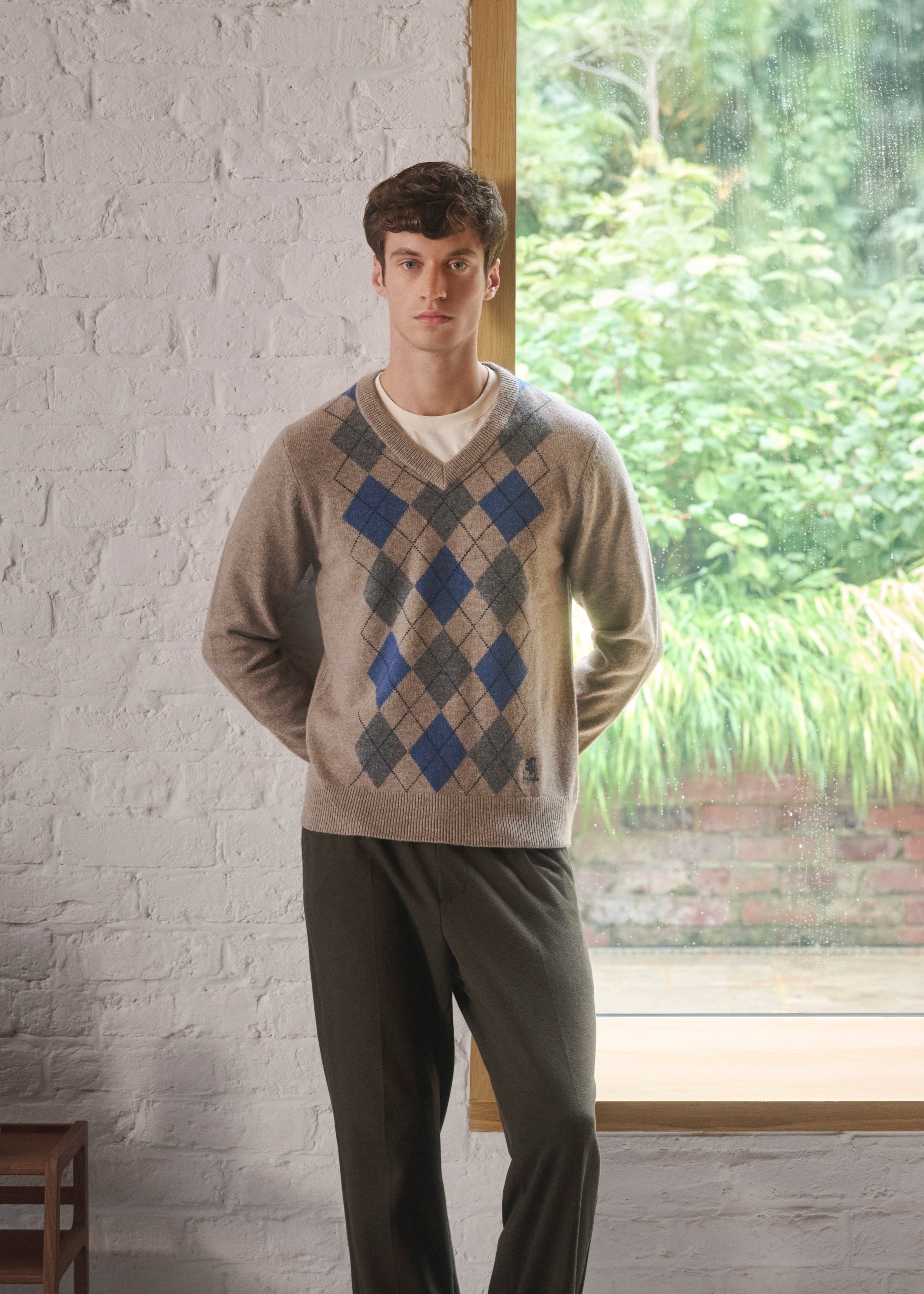 Man wearing a Pringle Argyle sweater standing in a room with a garden view