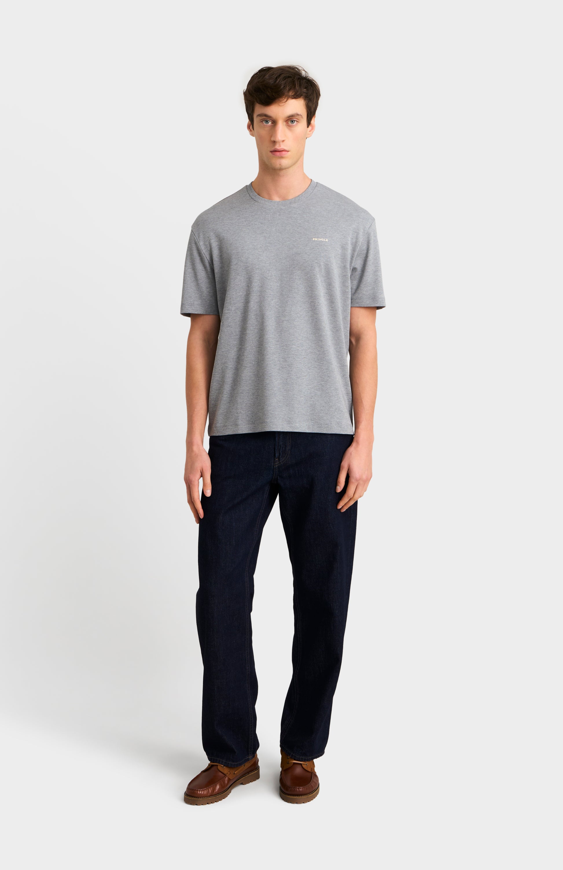 Man wearing a gray t-shirt and dark jeans on a white background