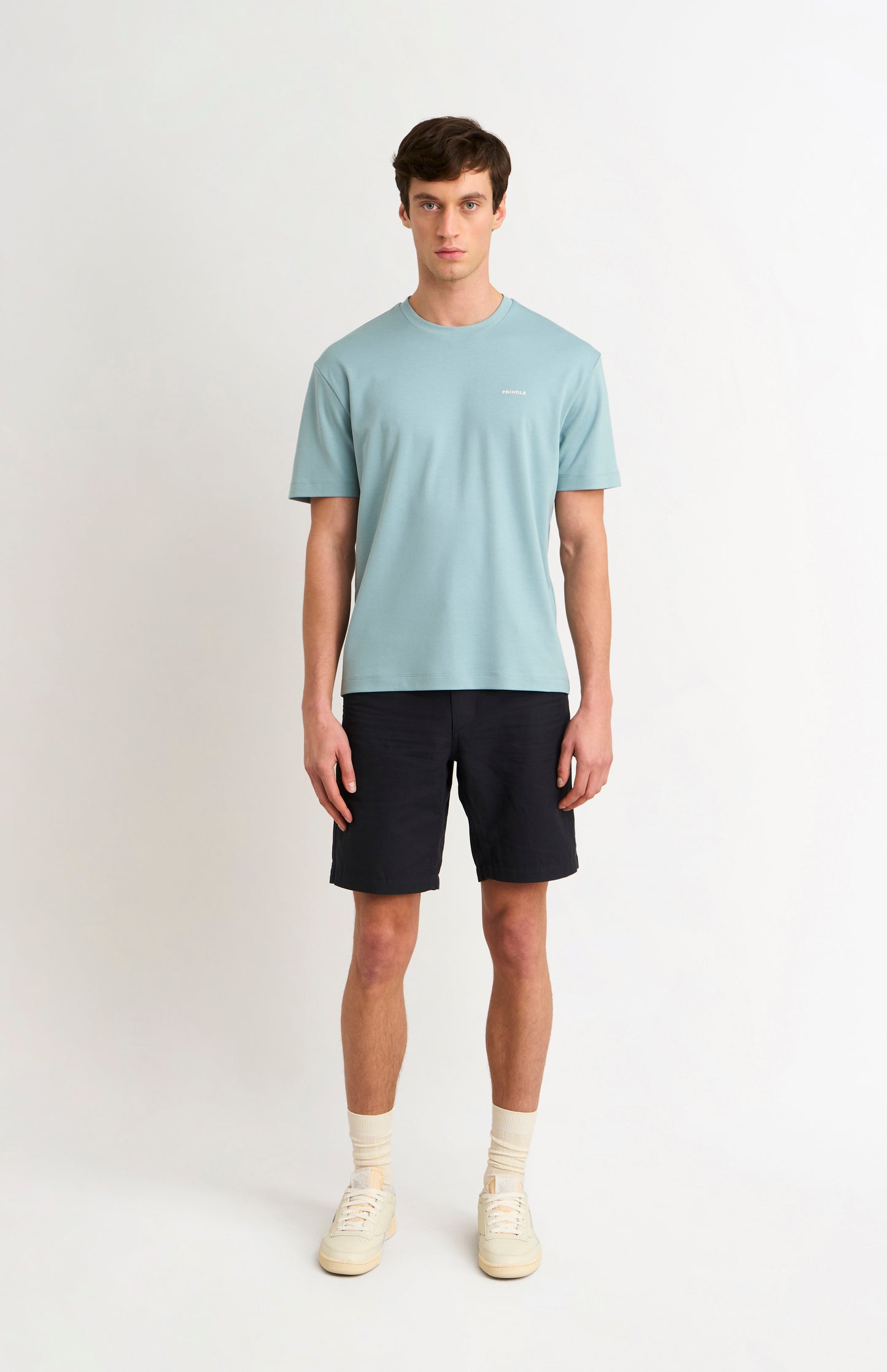 Man wearing a blue t-shirt and black shorts and white trainers on a white background