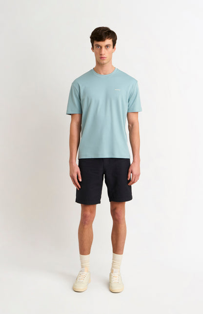 Man wearing a blue t-shirt and black shorts and white trainers on a white background