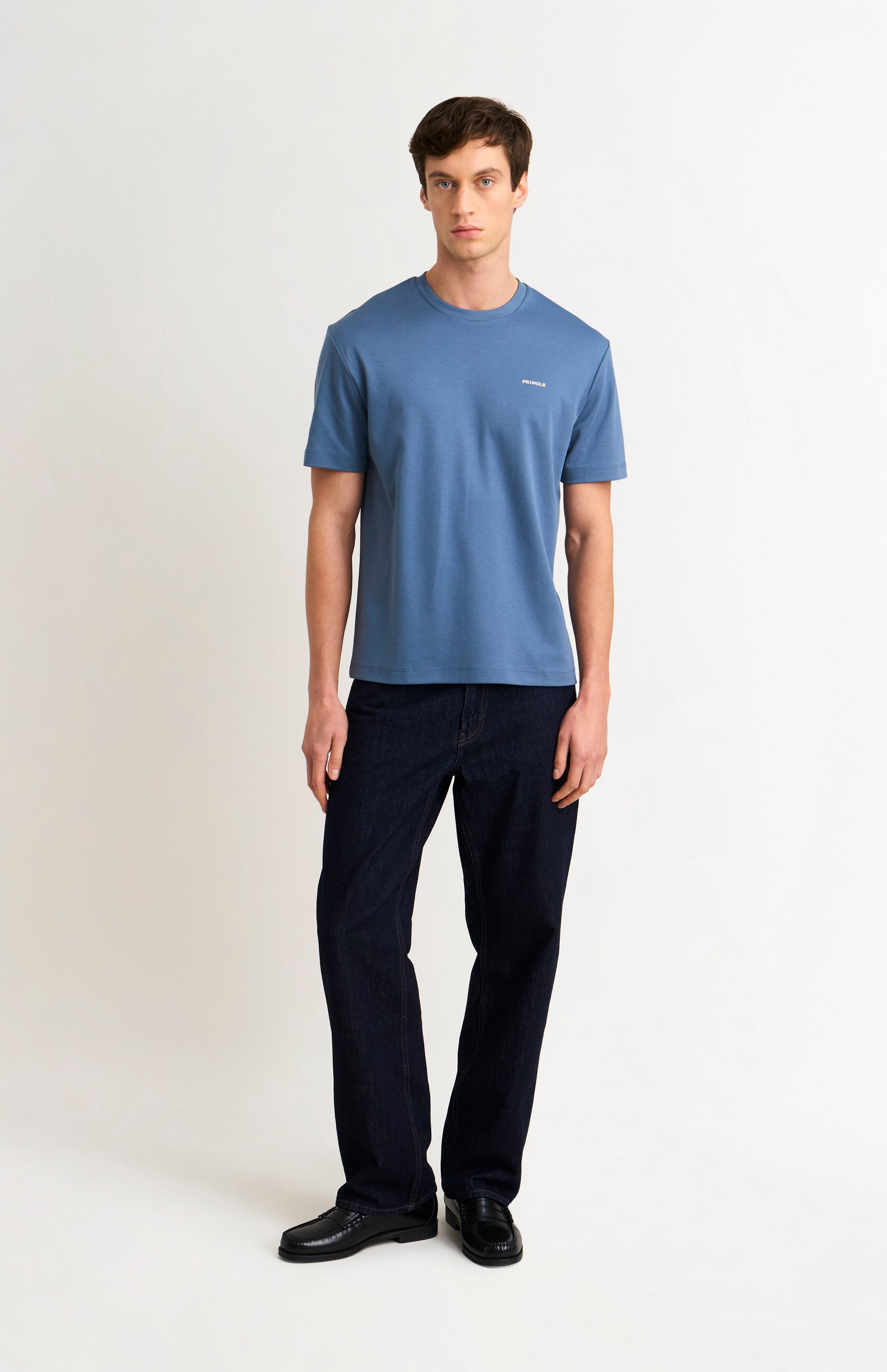 Man wearing a blue t-shirt and dark jeans on a white background