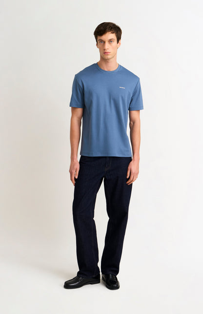 Man wearing a blue t-shirt and dark jeans on a white background