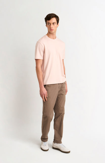 Man wearing a light pink t-shirt and beige trousers on a white background