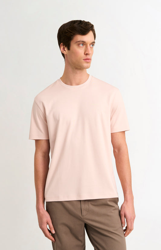 Man wearing a light pink t-shirt and beige trousers on a white background