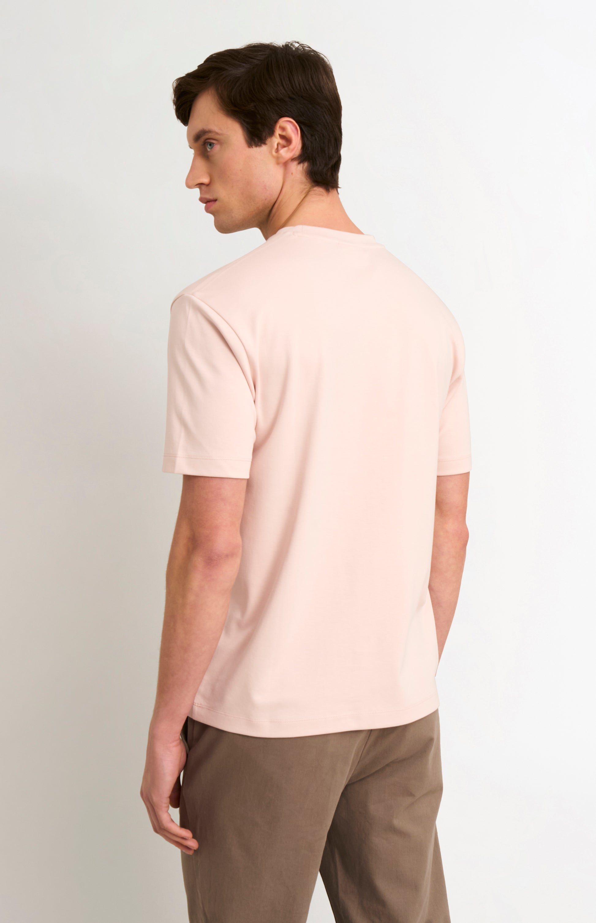 Man wearing a light pink t-shirt with beige trousers on a white background