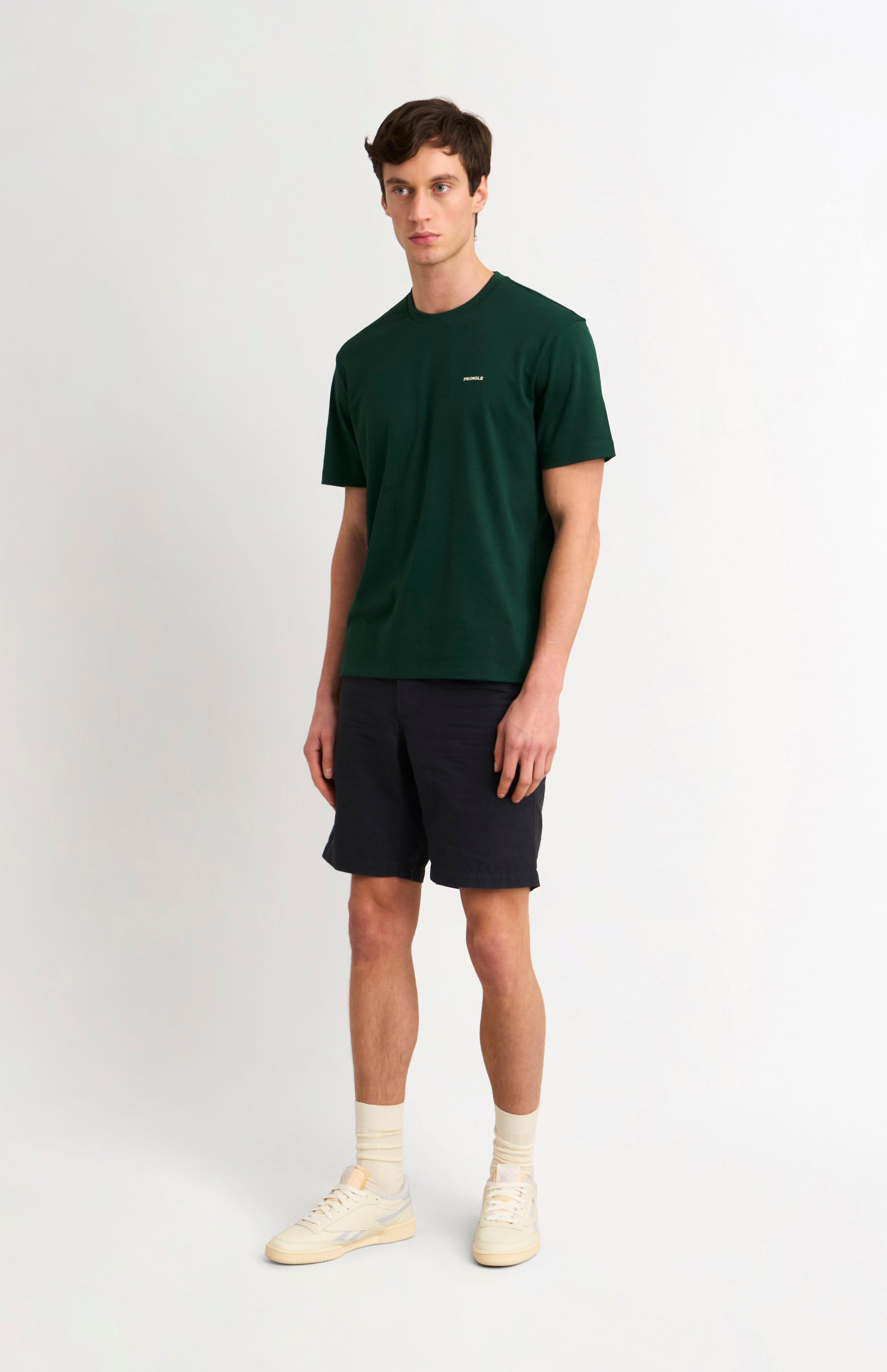 man wearing a dark green t-shirt and black shorts on a white background