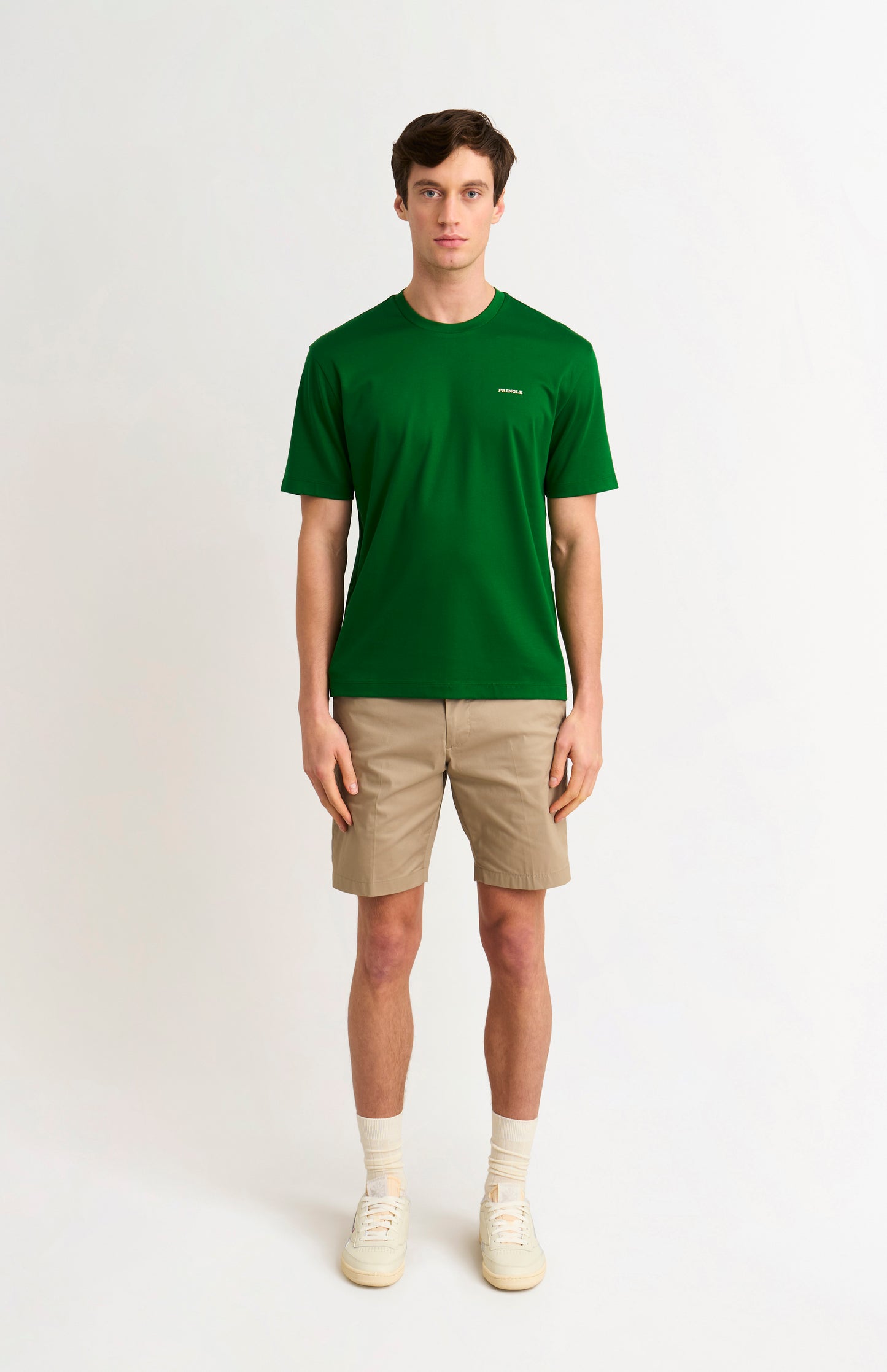 Man wearing a green t-shirt and beige shorts on a white background