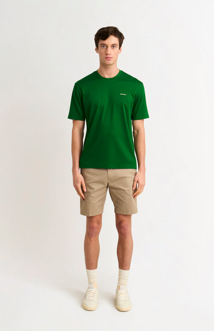 Man wearing a green t-shirt and beige shorts on a white background