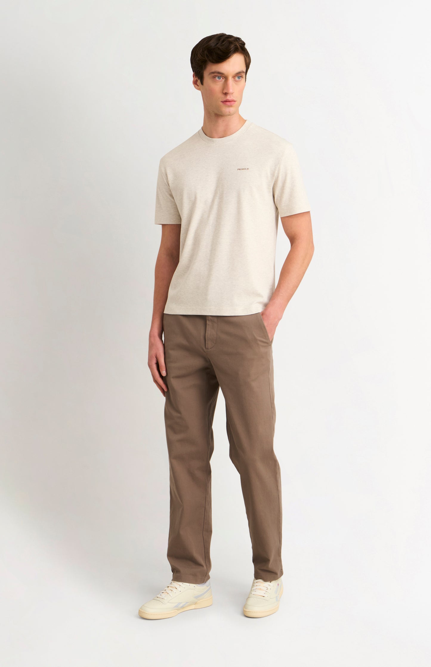 Man wearing an Ecru t-shirt and brown trousers on a white background