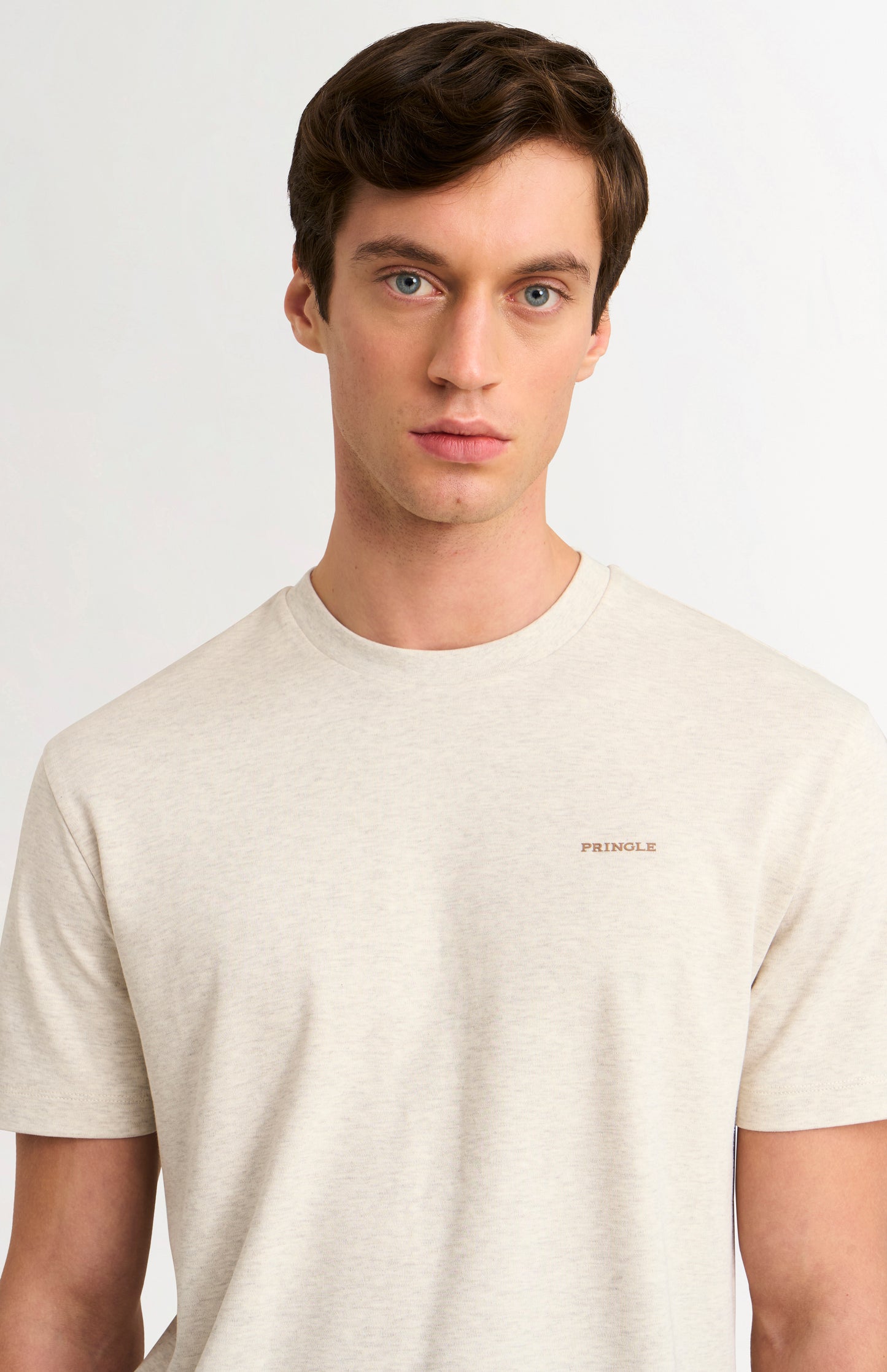 Man wearing a beige t-shirt with a brand logo on a light gray background