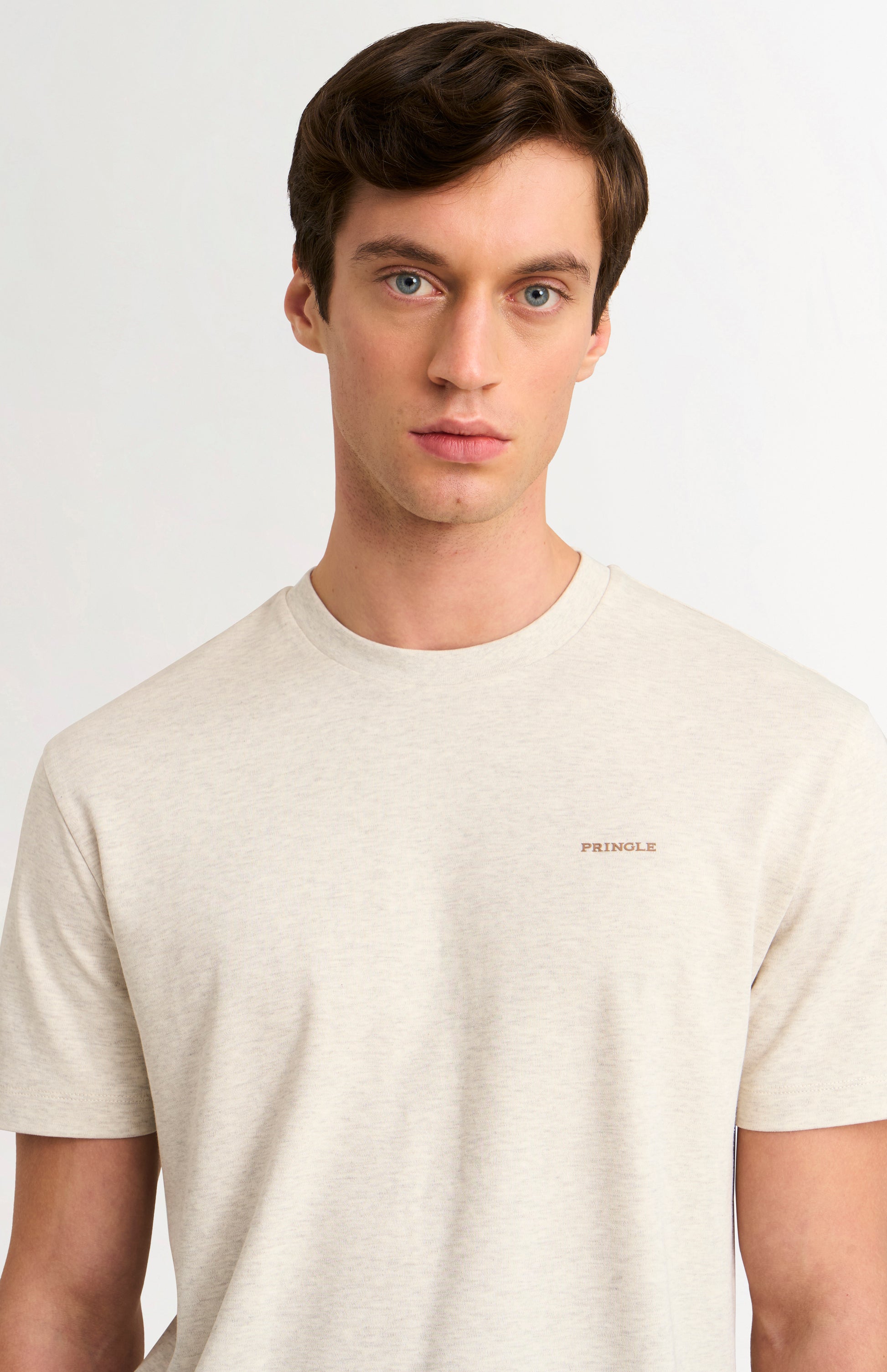 Man wearing a beige t-shirt with a brand logo on a light gray background