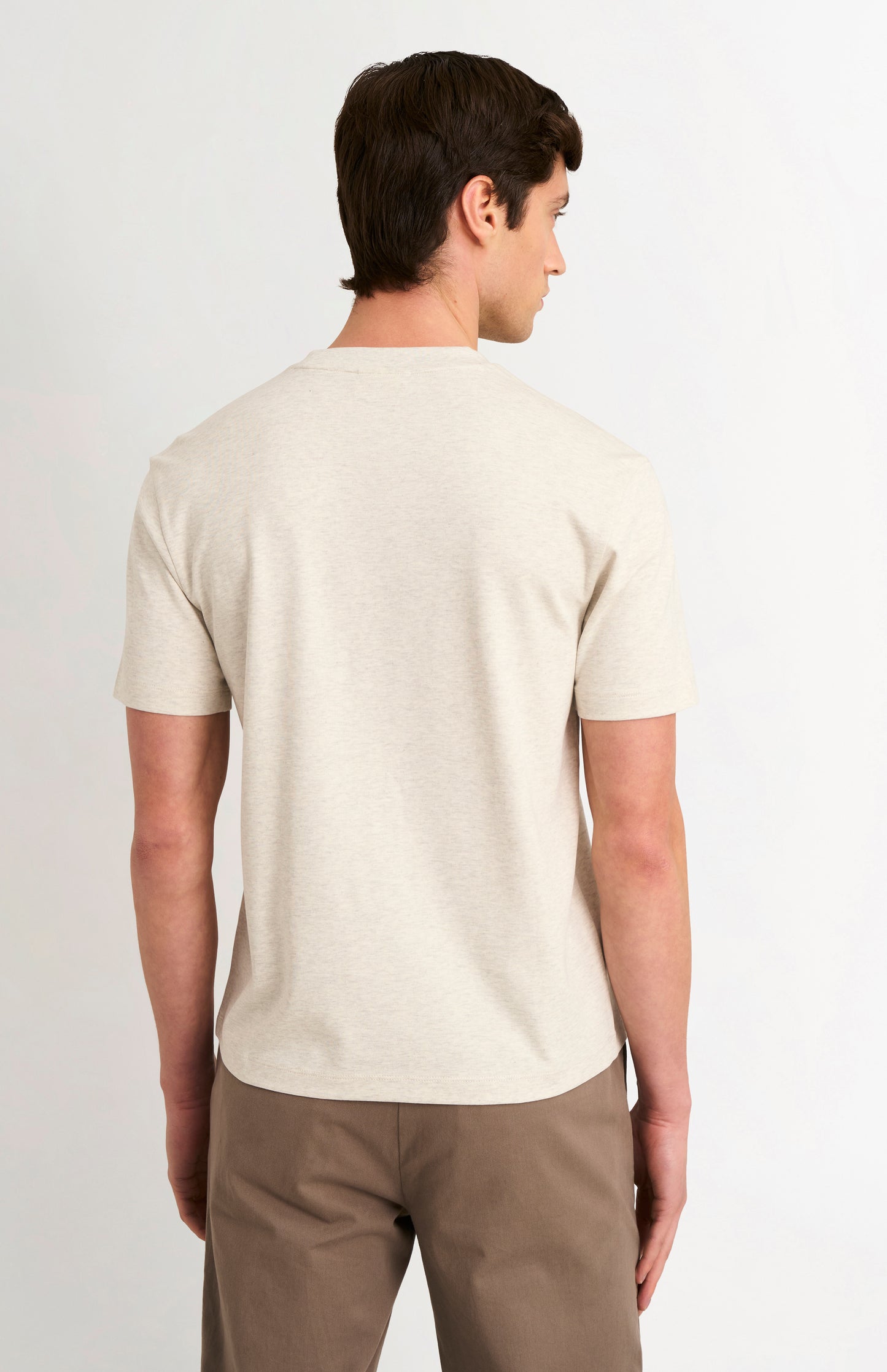 Man wearing a beige t-shirt and brown pants on a white background