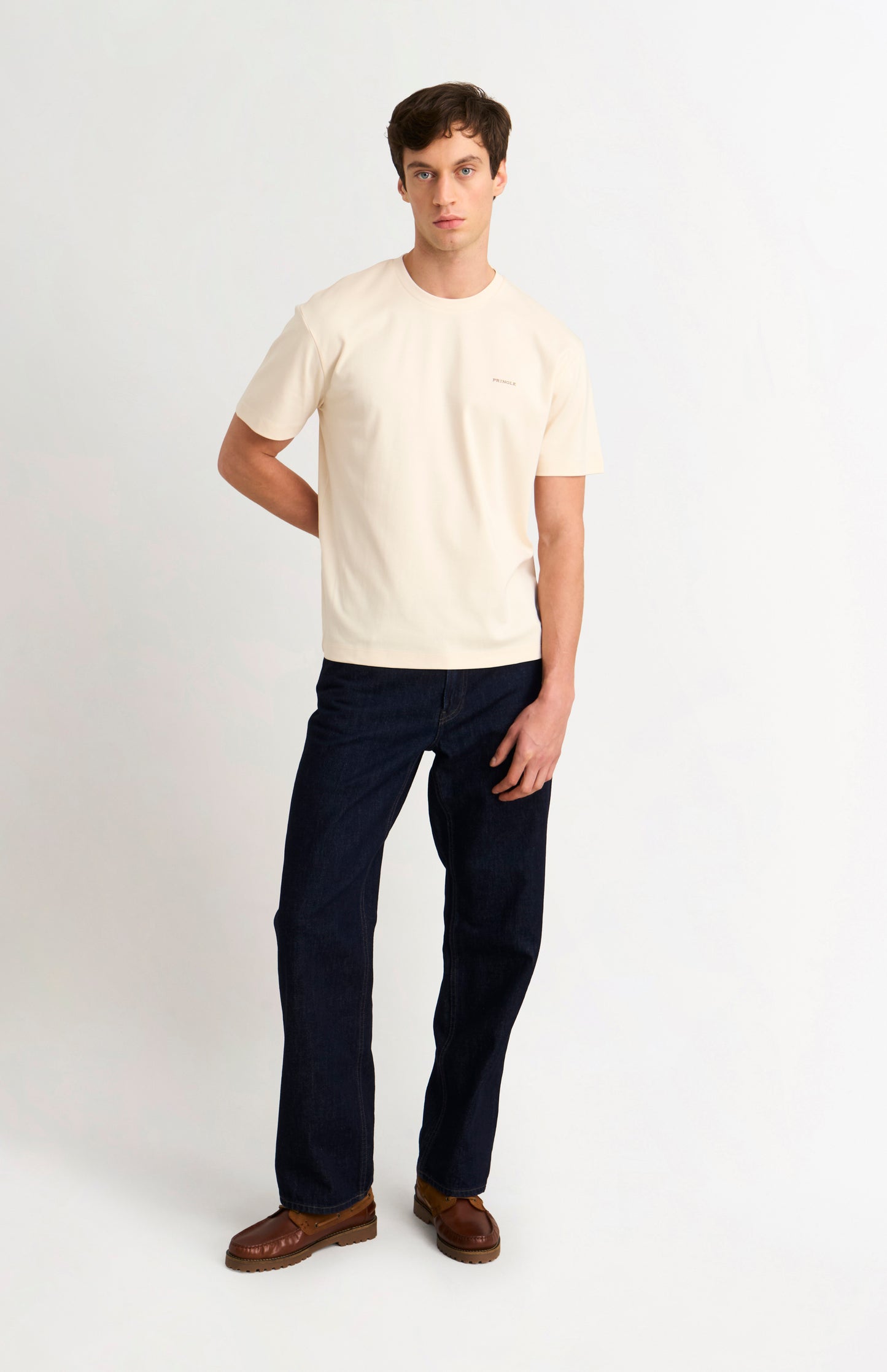 Man wearing an Ecru t-shirt and dark jeans on a white background