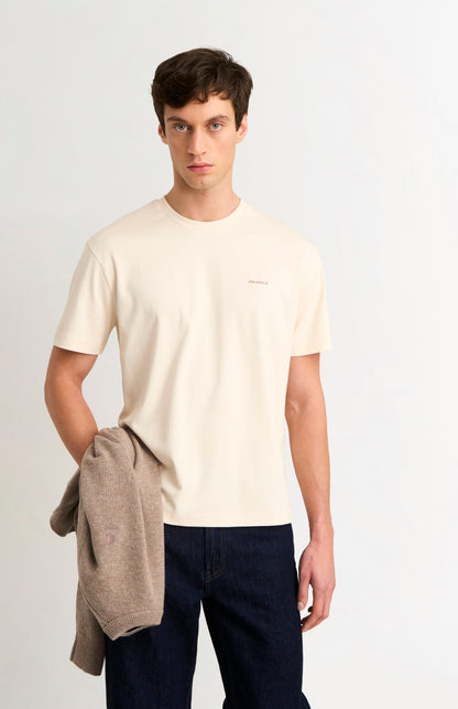 Man wearing an ecru t-shirt and dark jeans on a white background