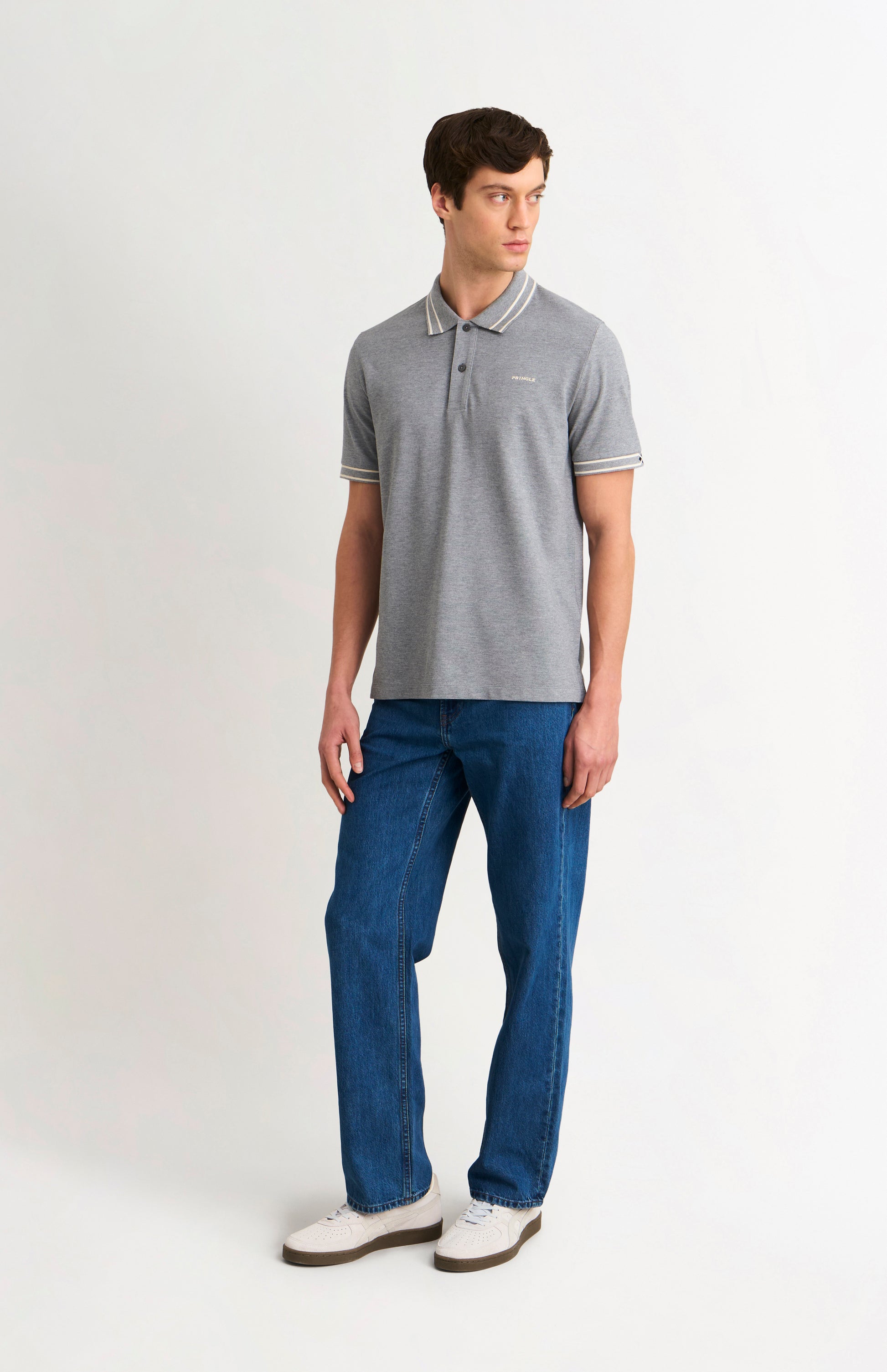 Man wearing a gray polo shirt and blue jeans on a white background
