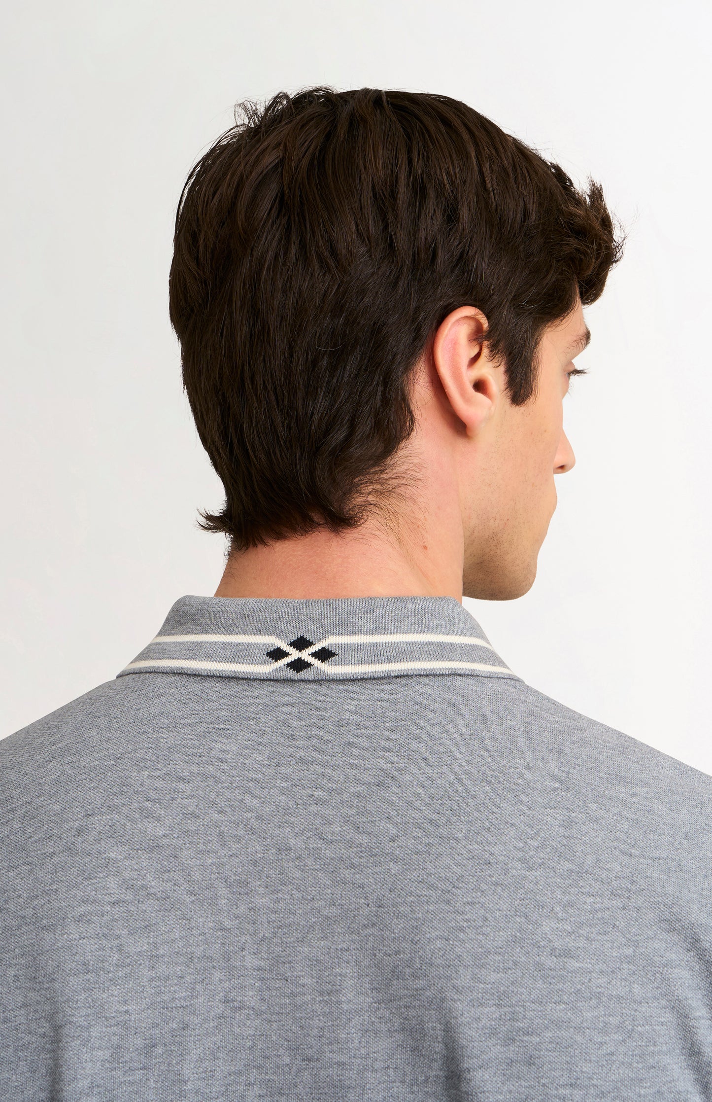 Man wearing a gray polo shirt with a brand logo on a white background