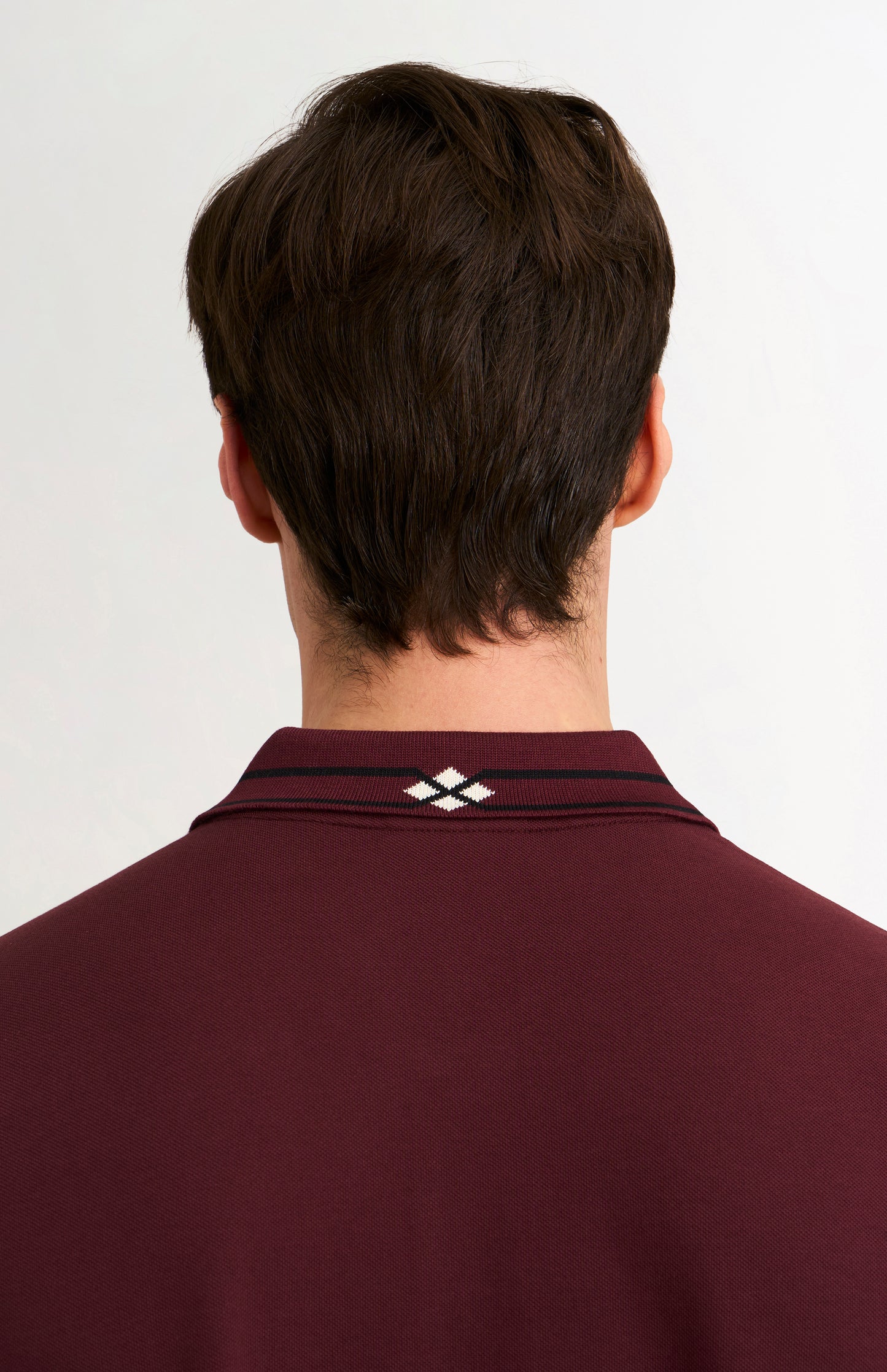 Detail shot of a burgundy polo shirt with black tipping details against a light grey background