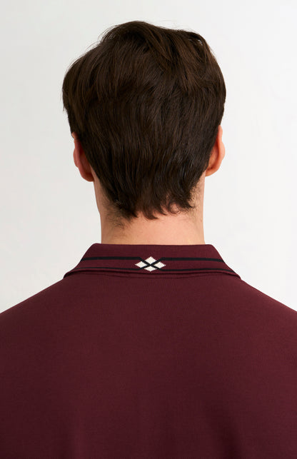 Detail shot of a burgundy polo shirt with black tipping details against a light grey background