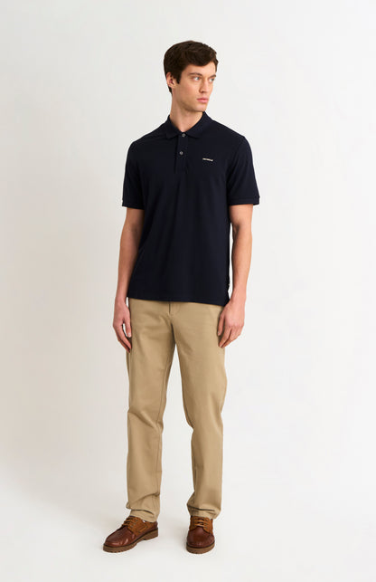 Man wearing a navy polo shirt and beige pants on a white background
