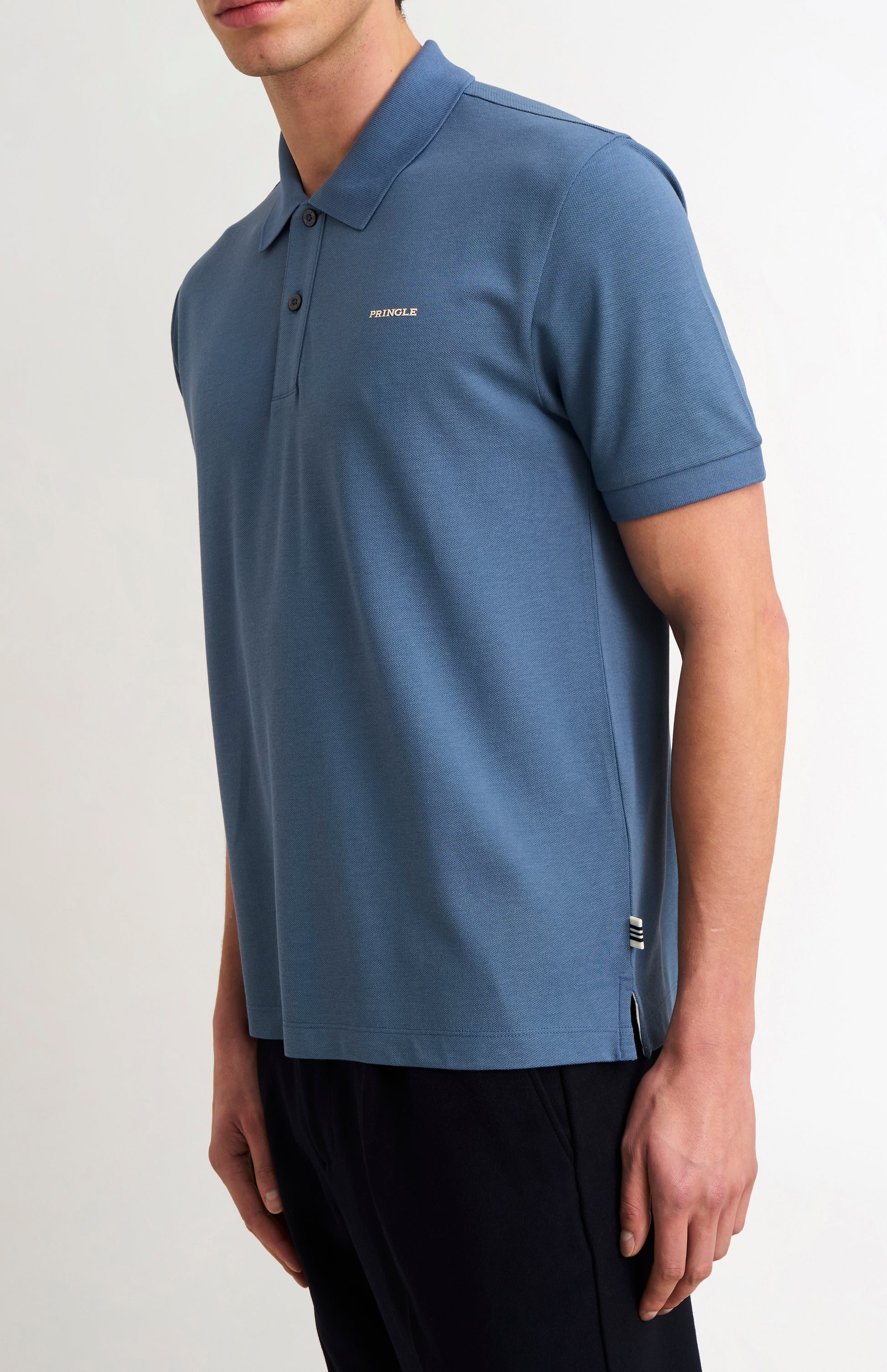 Man wearing a blue polo shirt with dark trousers on a white background