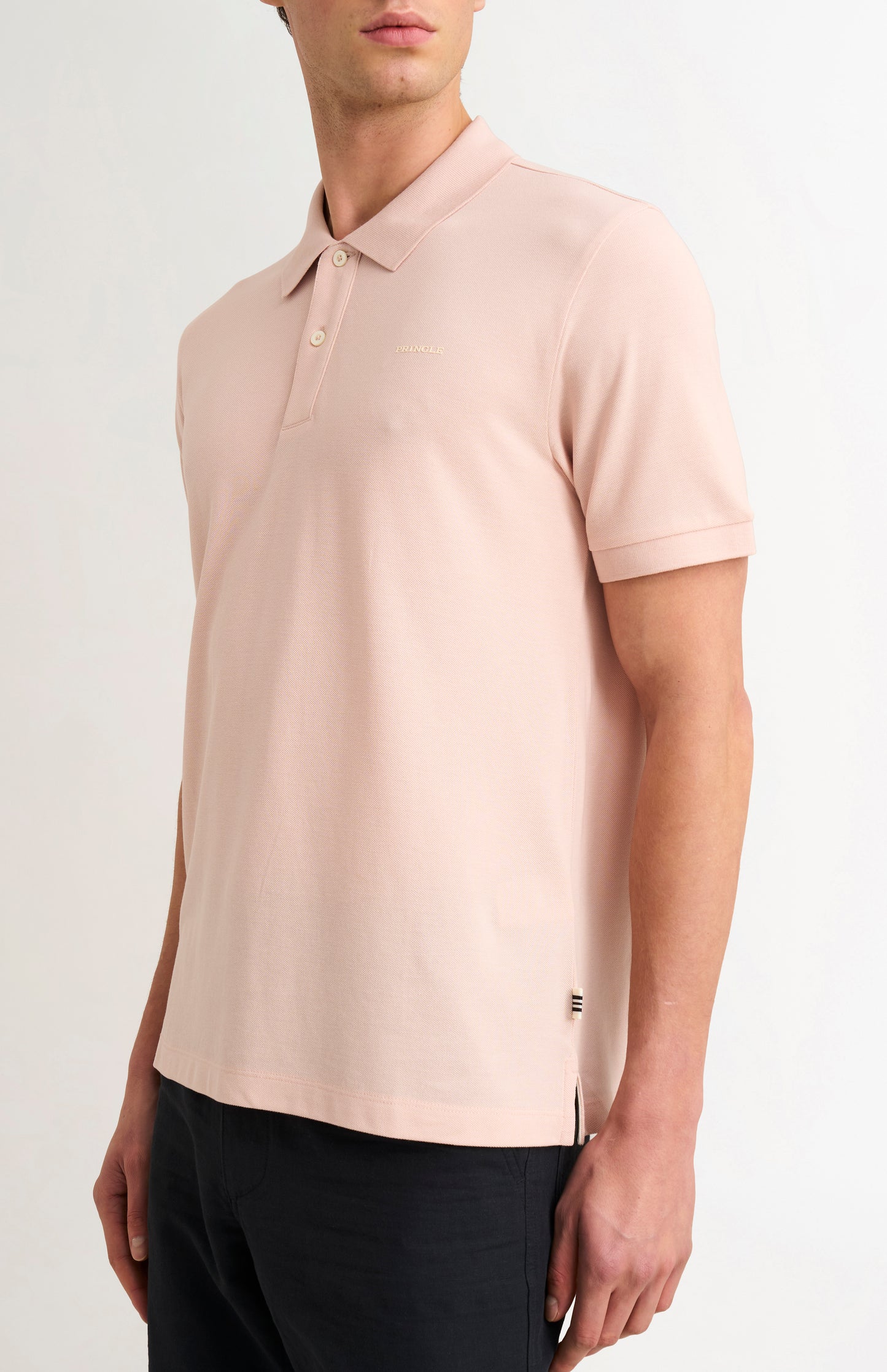 Man wearing a light pink polo shirt with a brand logo on a white background