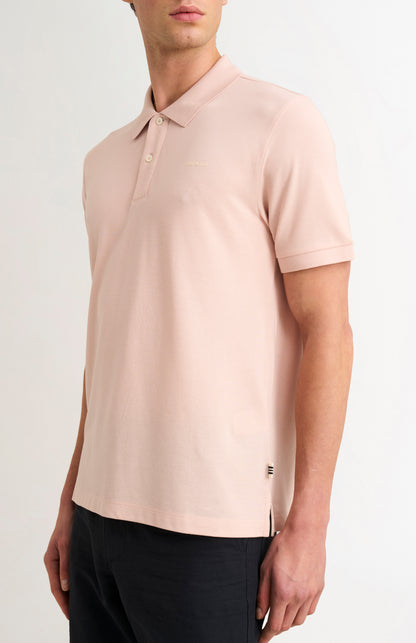 Man wearing a light pink polo shirt with a brand logo on a white background