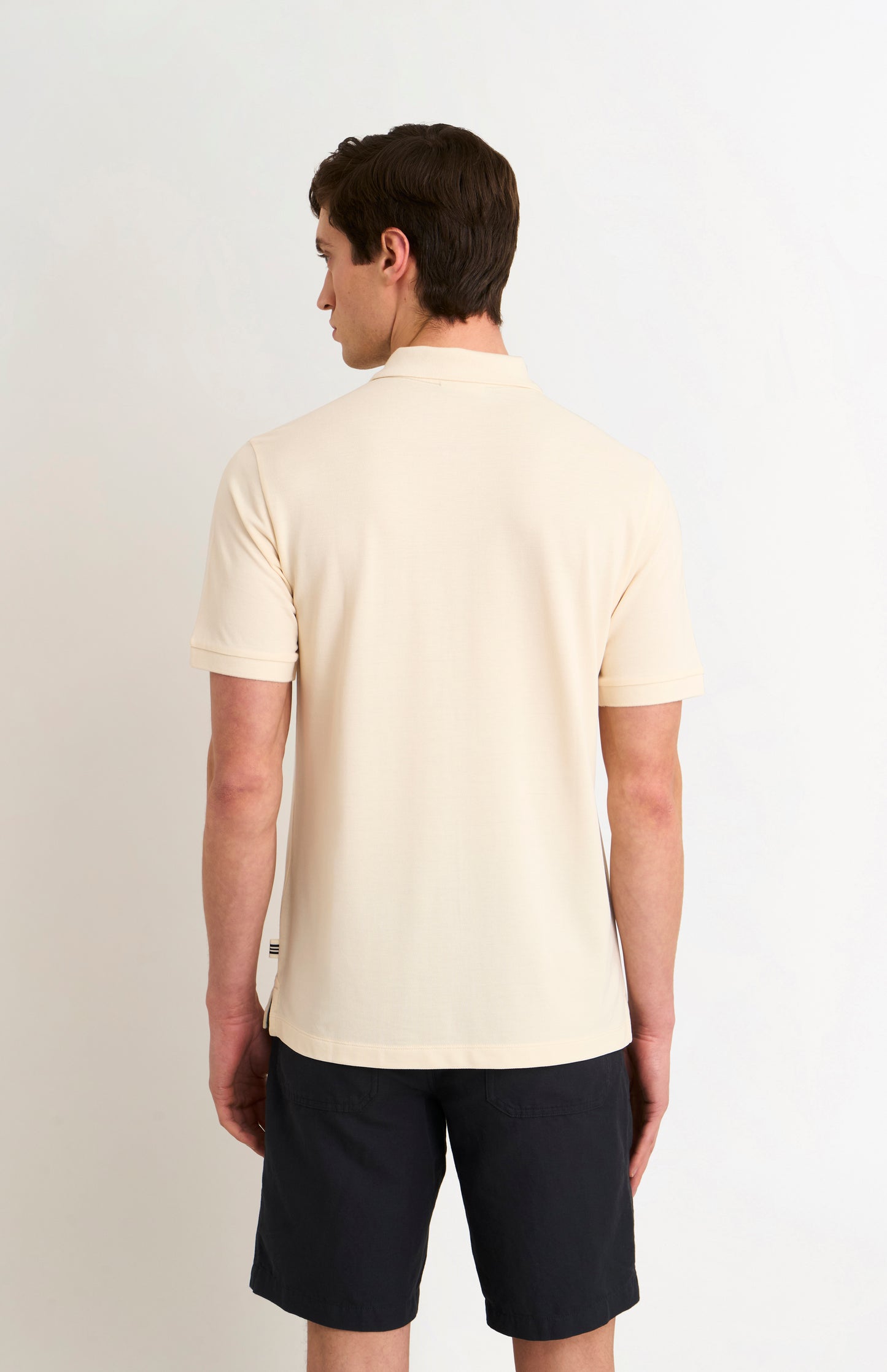 Man wearing a beige polo shirt and black shorts on a white background
