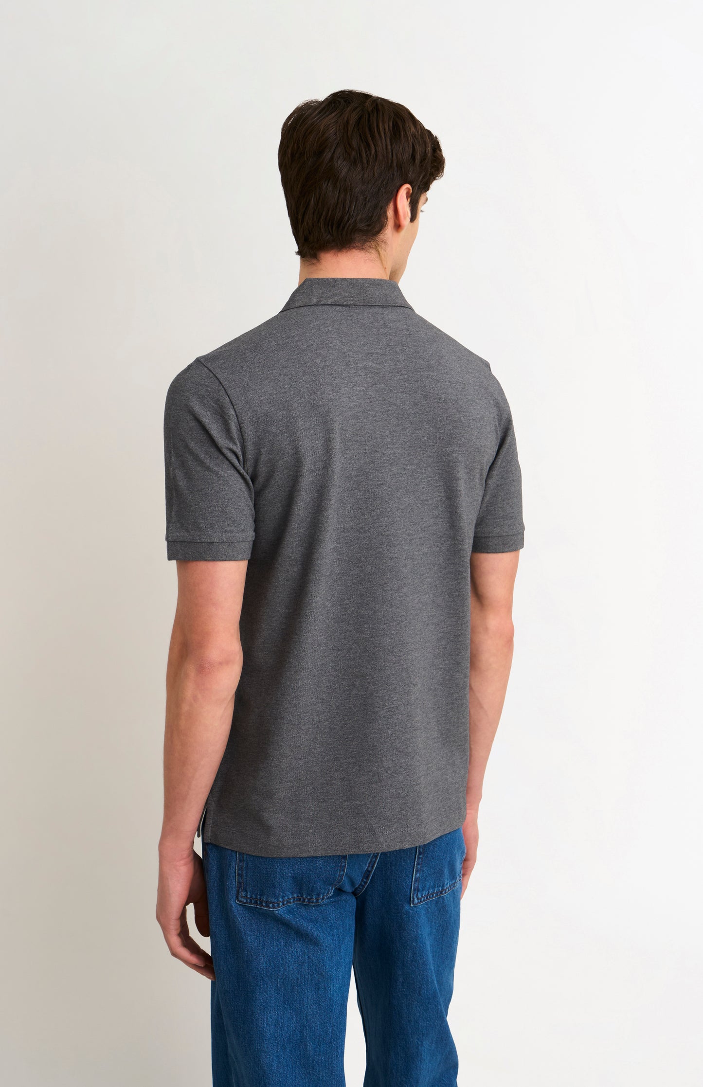 Man wearing a gray polo shirt and blue jeans on a white background