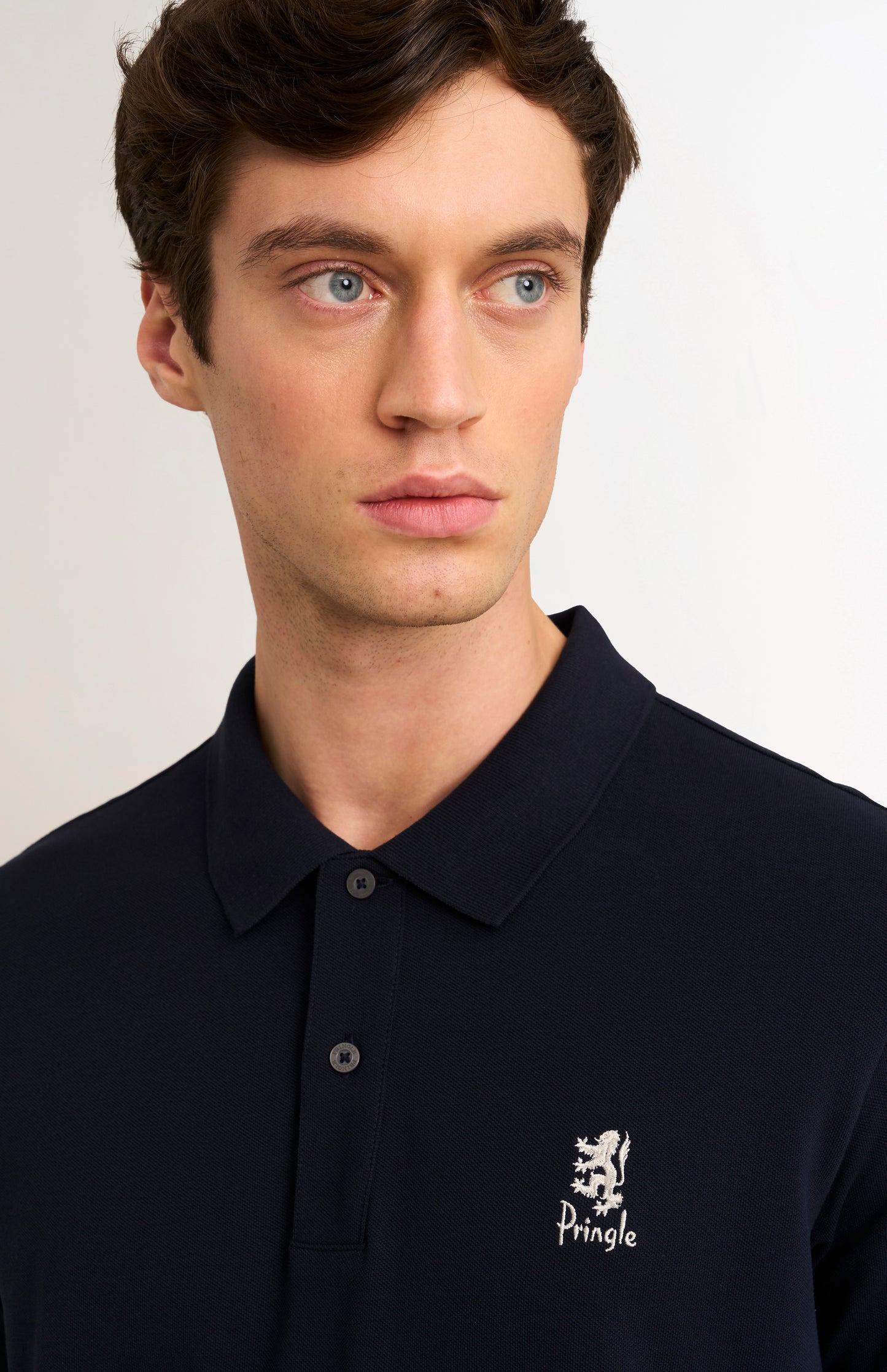 Man wearing a navy blue polo shirt with a brand logo on a plain background