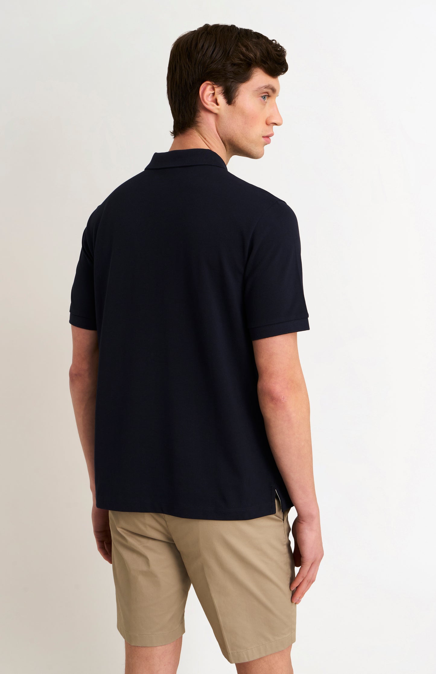 Man wearing a navy polo shirt and beige shorts on a light background