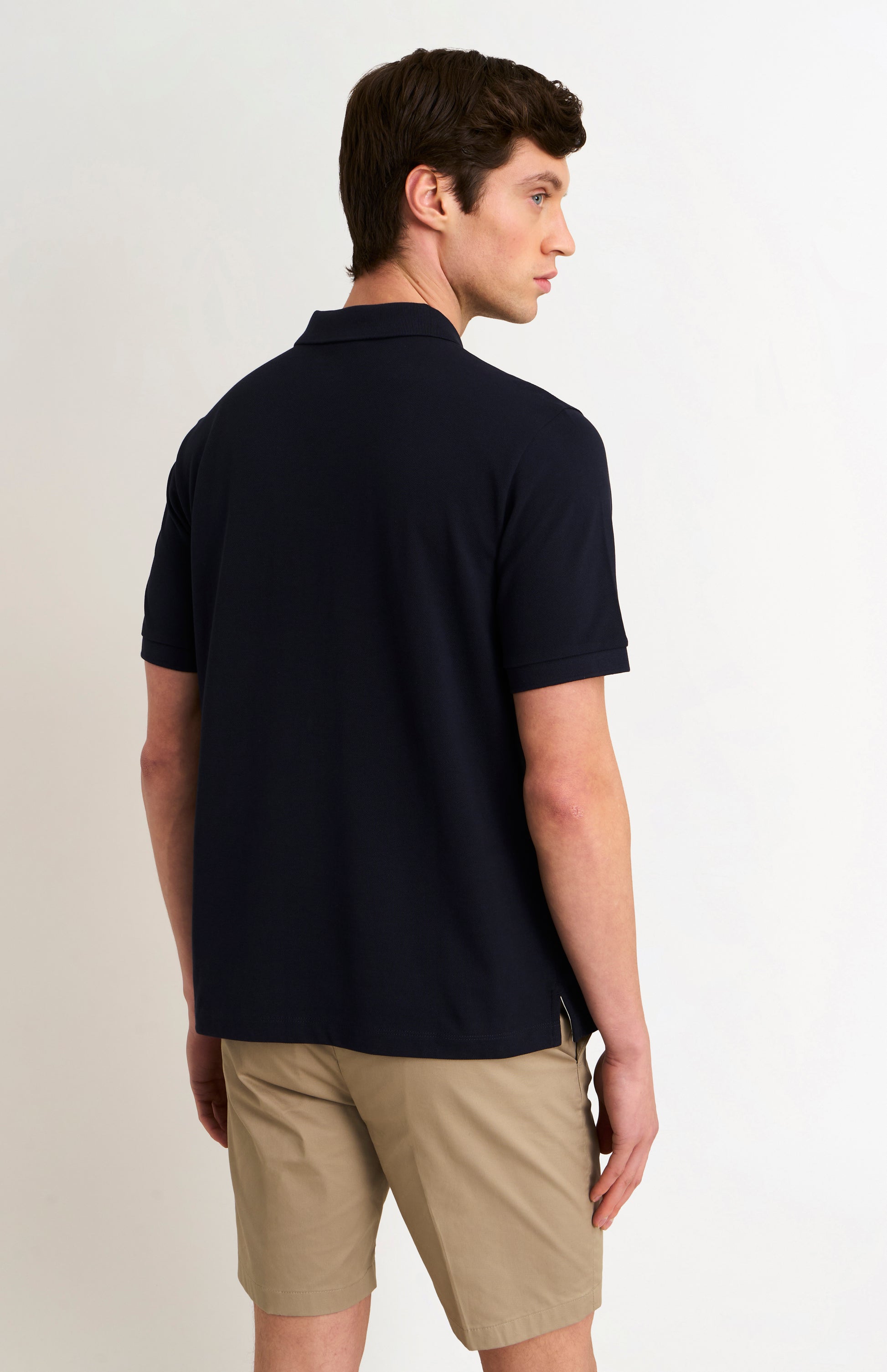 Man wearing a navy polo shirt and beige shorts on a light background
