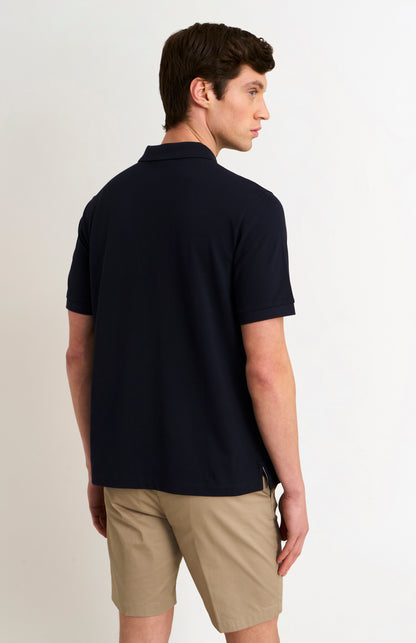 Man wearing a navy polo shirt and beige shorts on a light background
