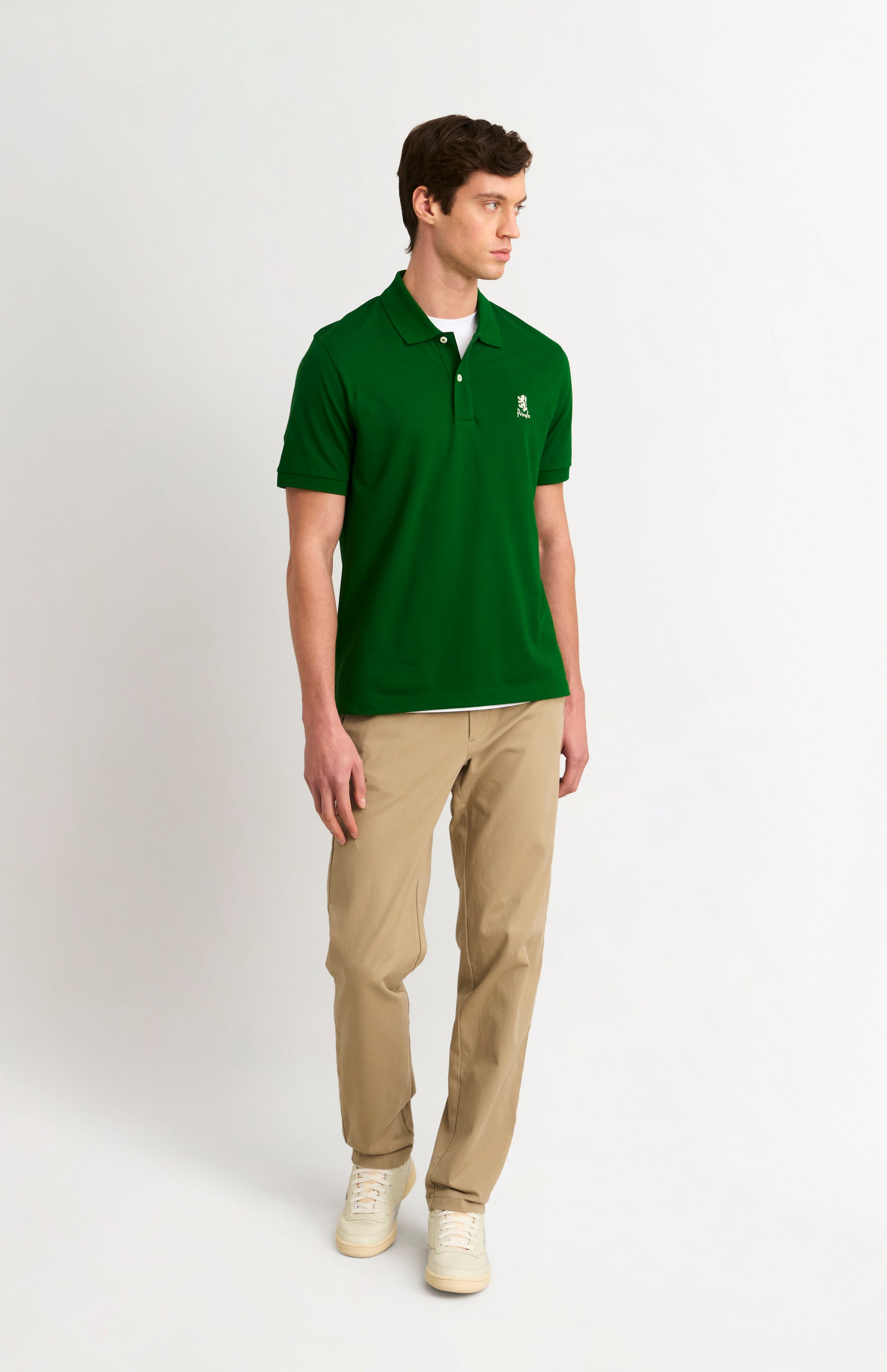 Man wearing a green polo shirt and beige pants on a white background