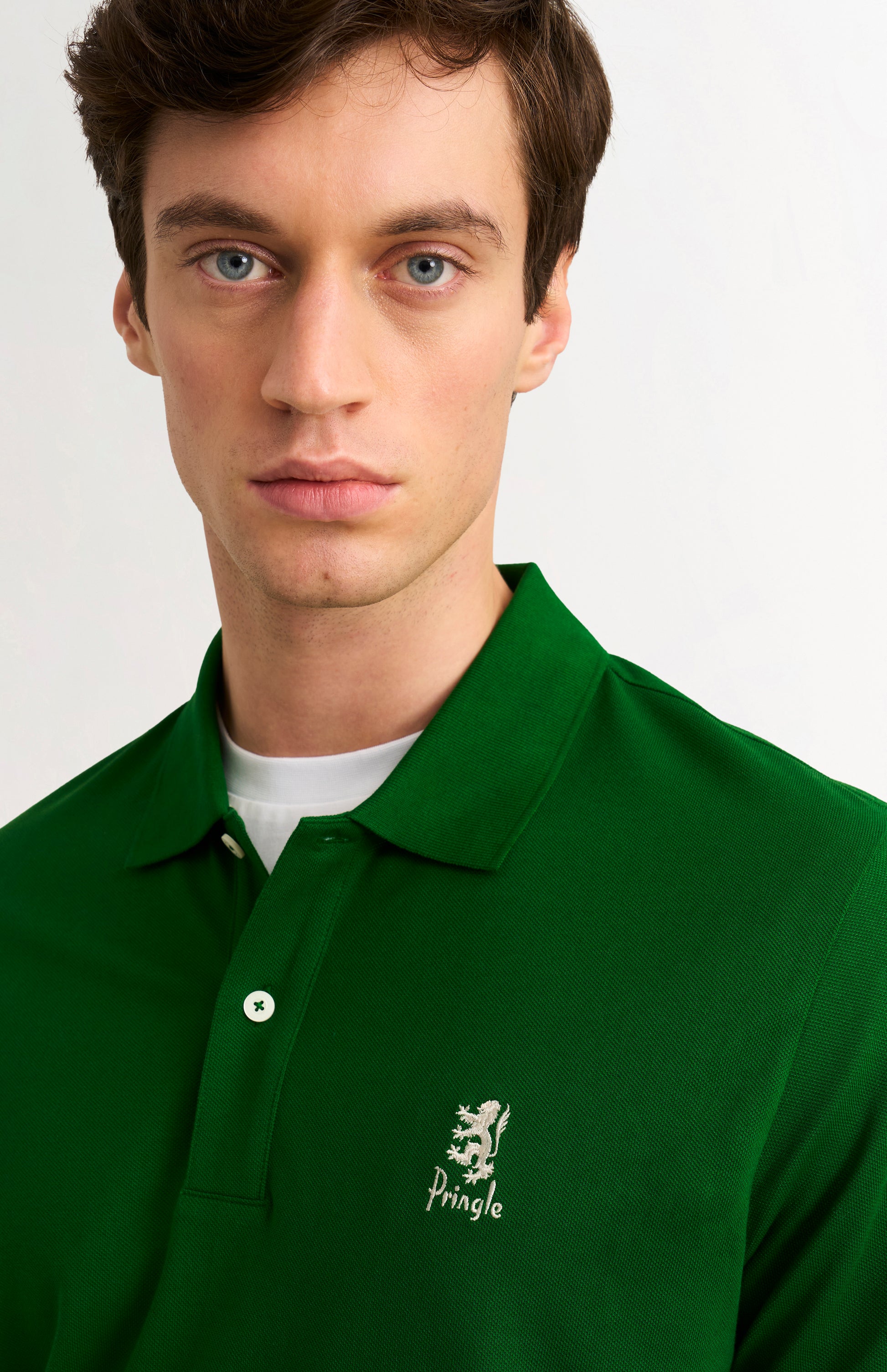 Man wearing a green polo shirt with a brand logo on a plain background