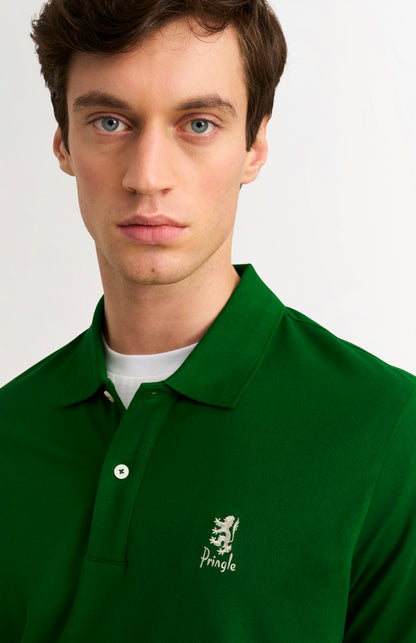 Man wearing a green polo shirt with a brand logo on a plain background