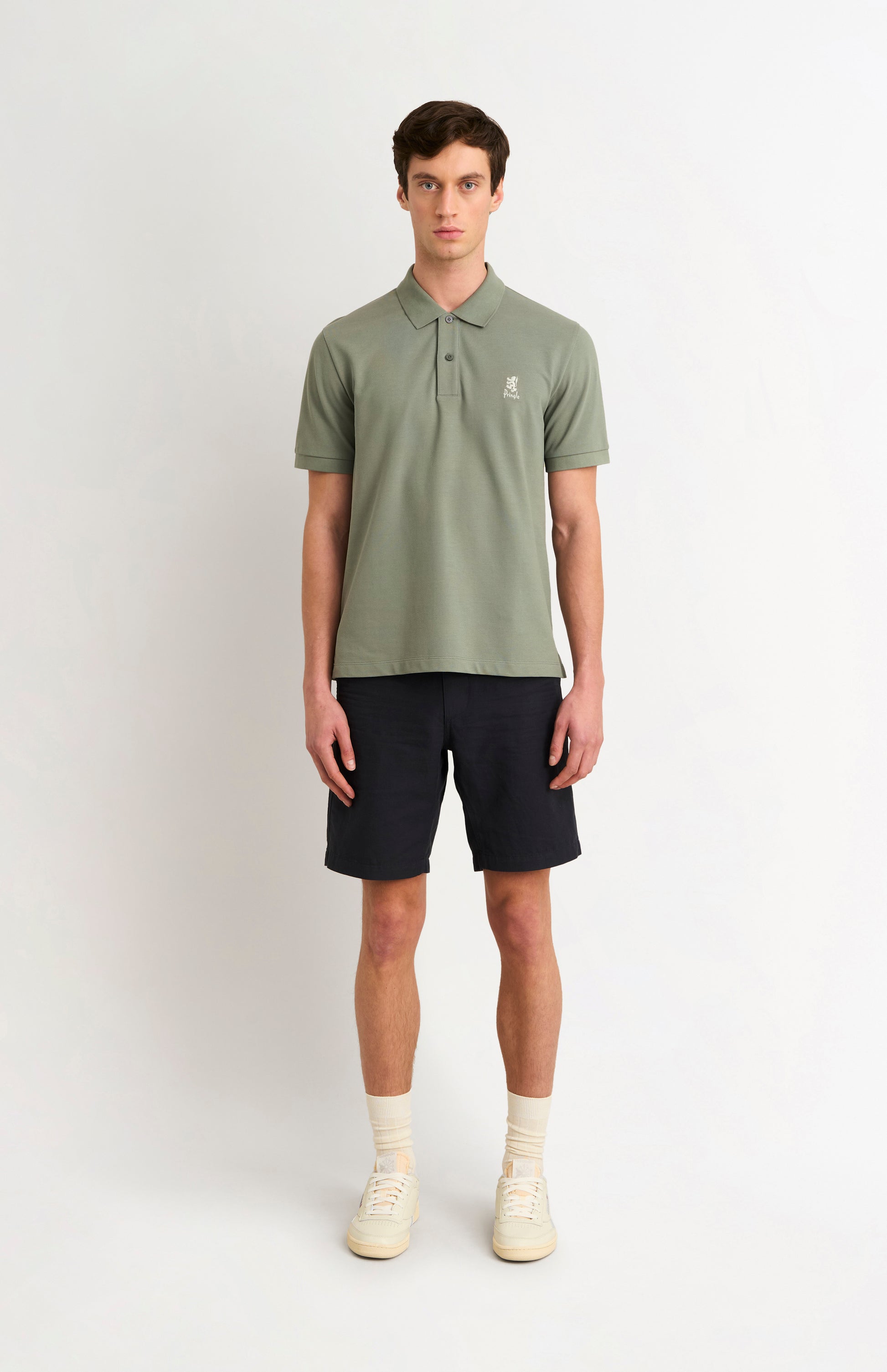Man wearing a green polo shirt and black shorts on a white background