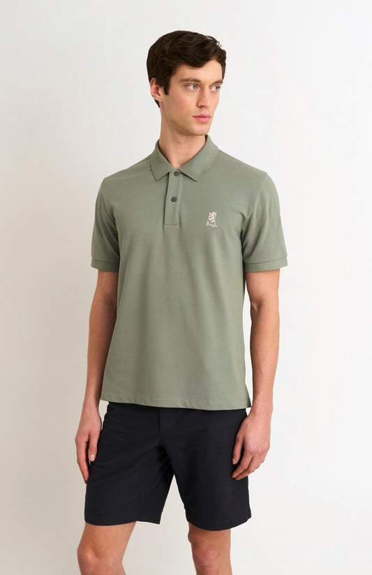 Man wearing a green polo shirt with a logo on a plain background