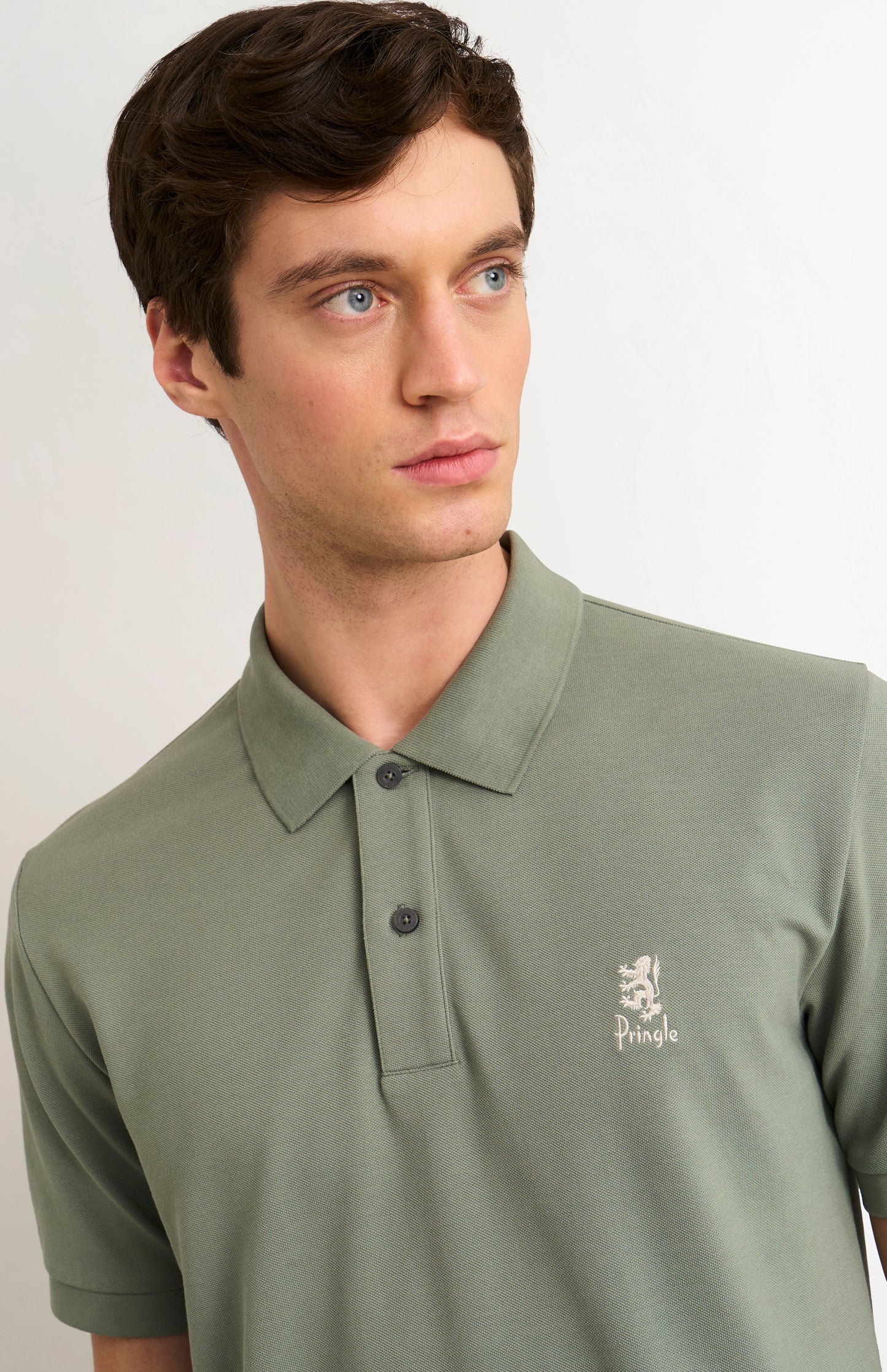 Man wearing a green polo shirt with a brand logo on a plain background