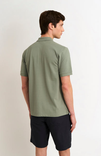 Man wearing a green polo shirt and black shorts on a plain background