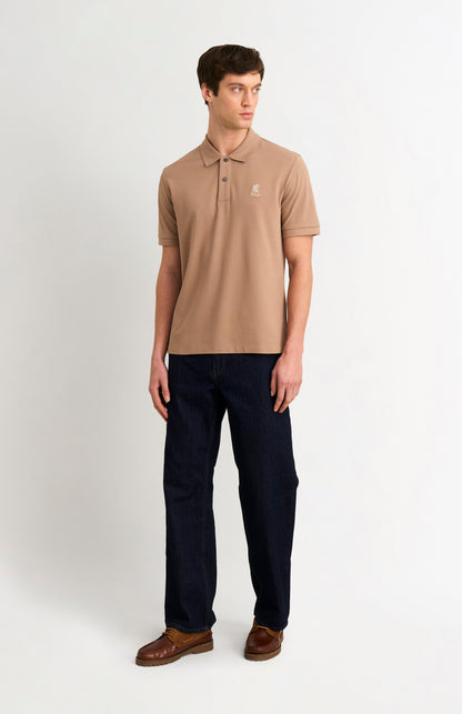 Man wearing a brown polo shirt and dark pants on a white background
