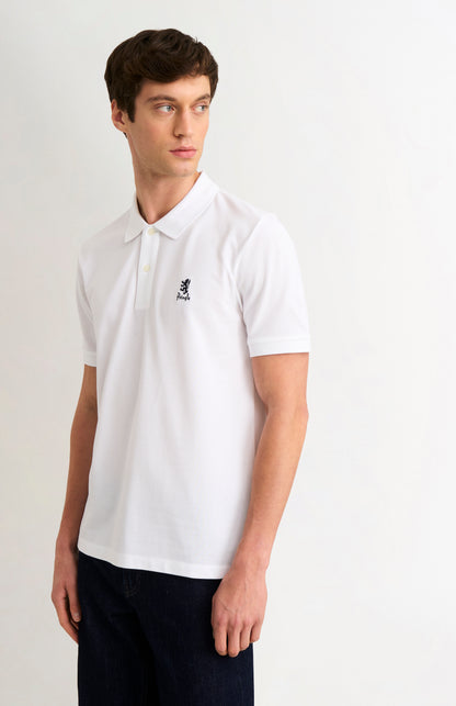 Man wearing a white polo shirt with a logo on a plain background