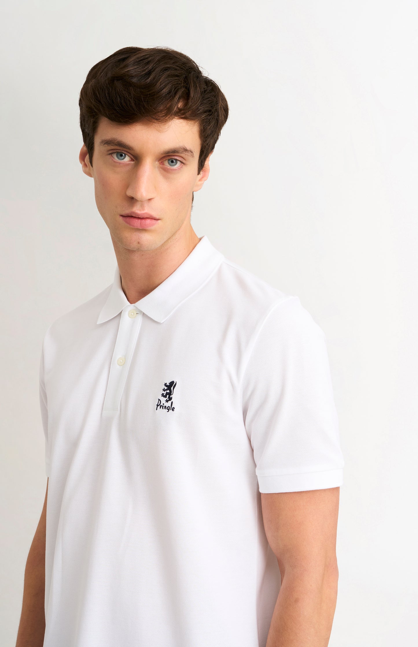 Man wearing a white polo shirt with a small logo on a plain background