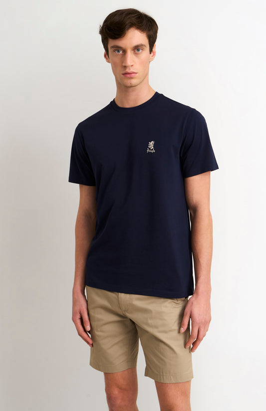Man wearing a navy t-shirt with a small logo and beige shorts on a white background