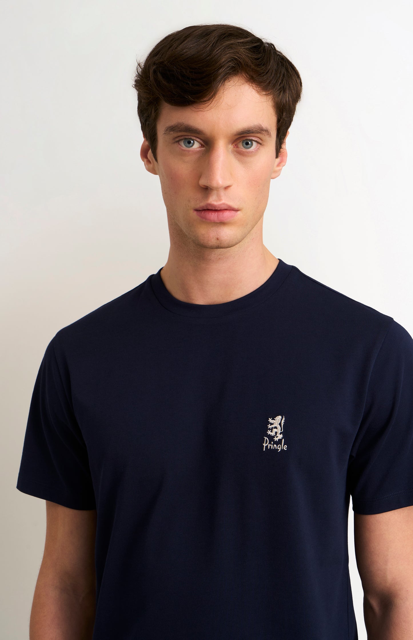 Man wearing a navy blue t-shirt with a small logo on a plain background