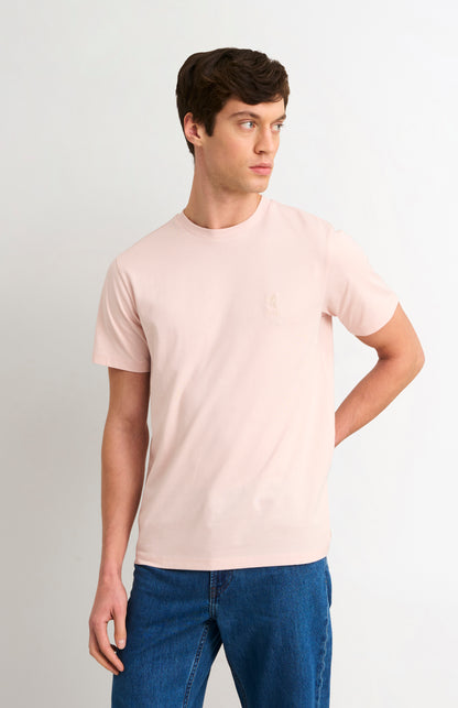 Man wearing a light pink t-shirt and blue jeans against a plain background