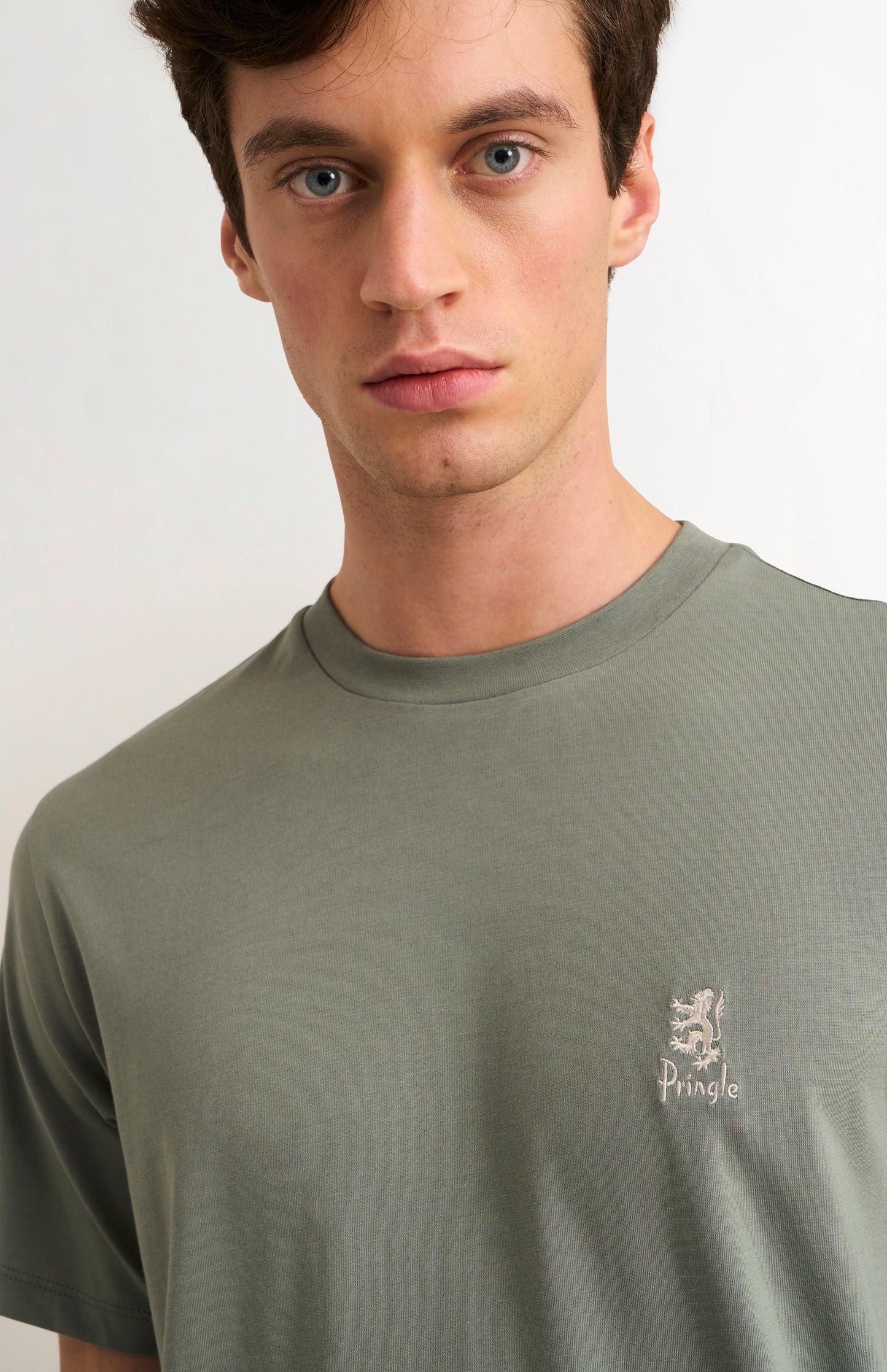 Man wearing a green t-shirt with a small logo on a white background