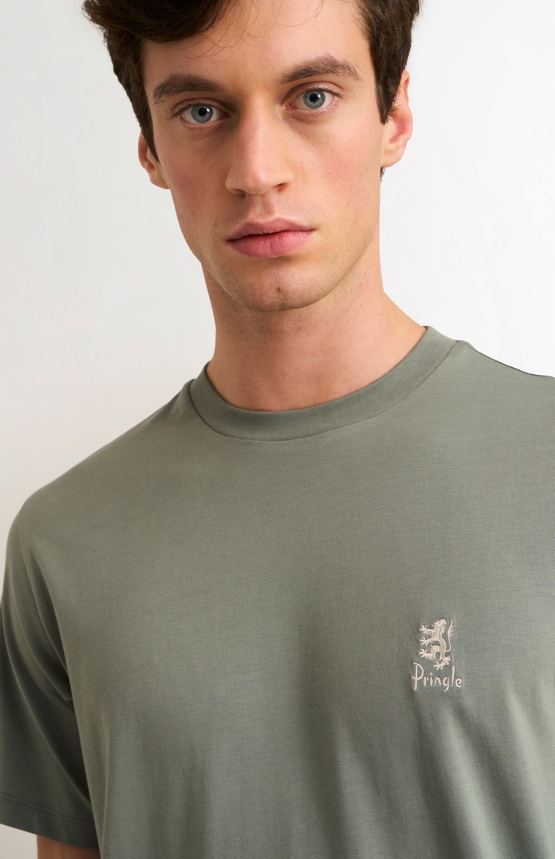 Man wearing a green t-shirt with a small logo on a white background