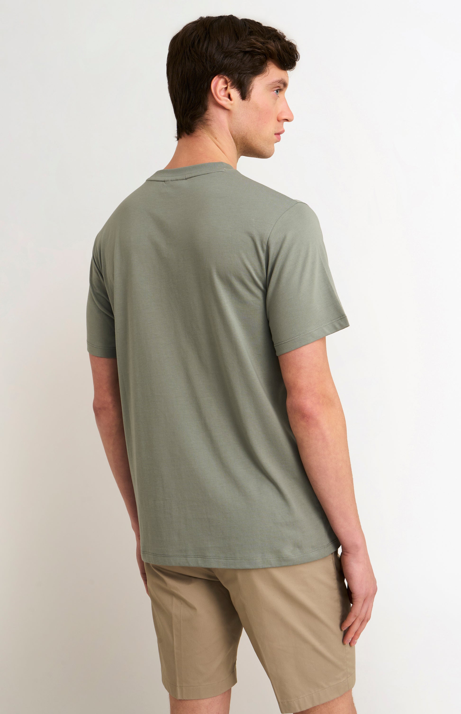 Man wearing a green t-shirt and beige shorts on a white background