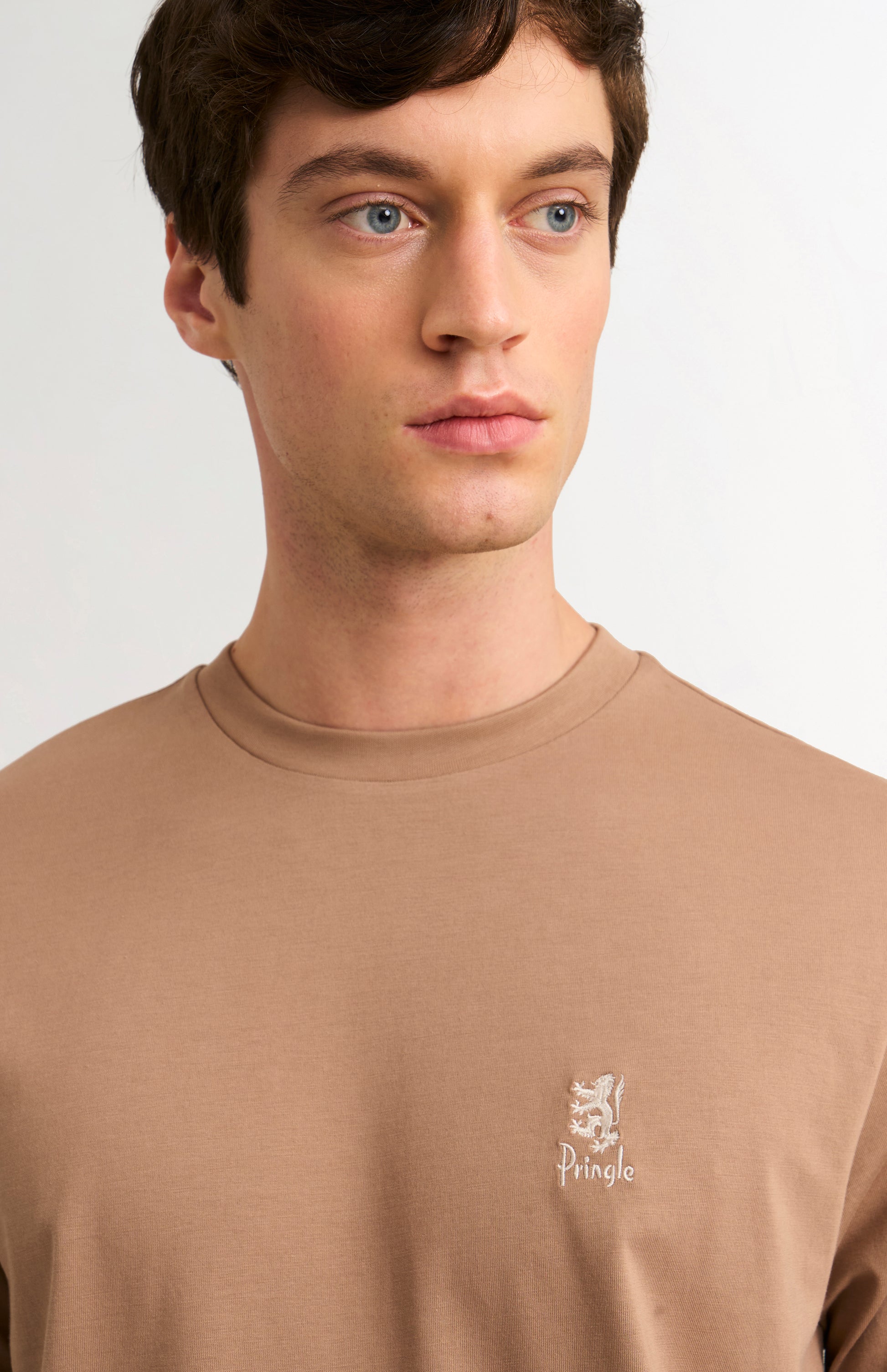 Man wearing a brown t-shirt with a small logo on a plain background