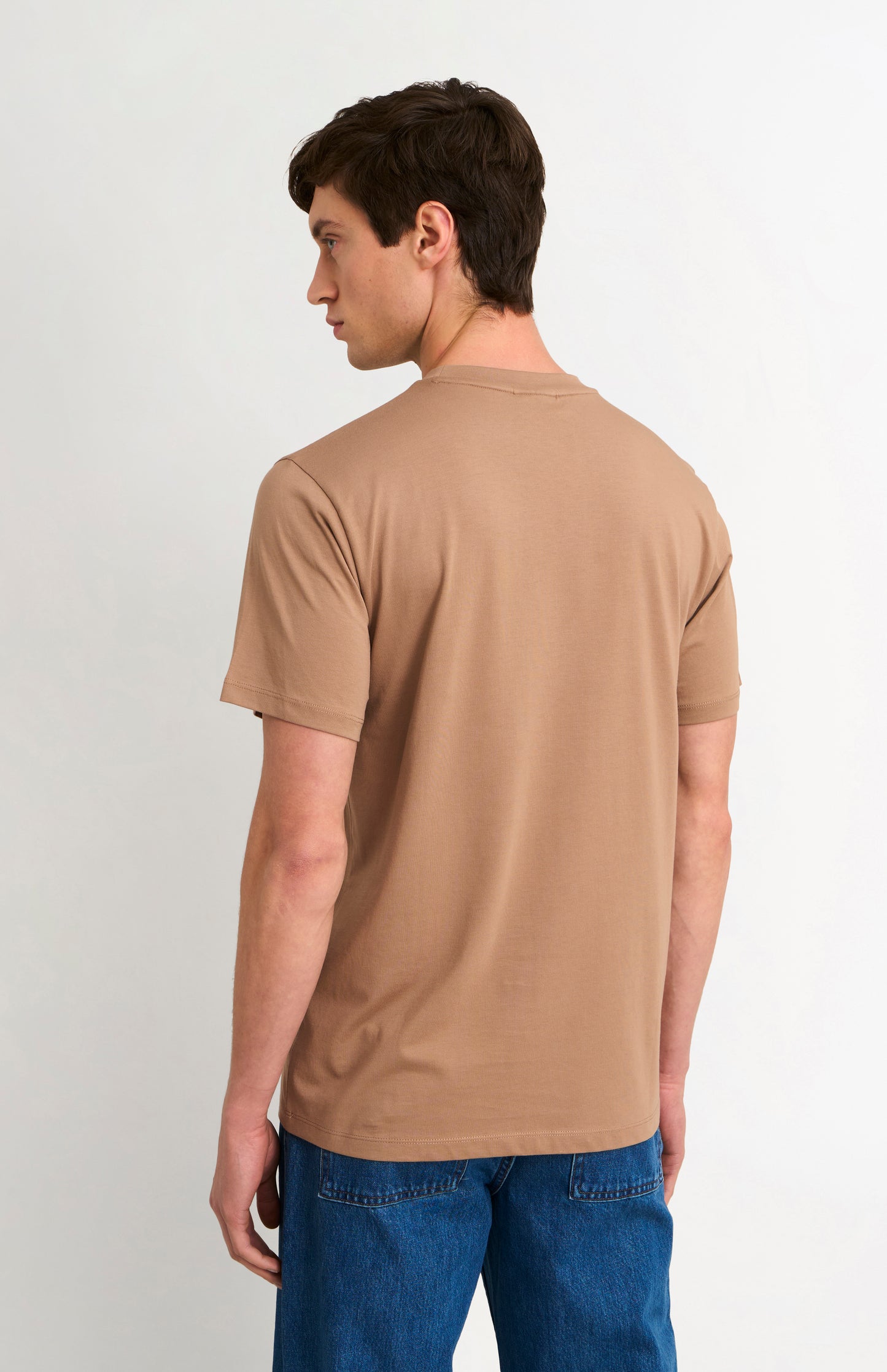 Man wearing a brown t-shirt and blue jeans on a white background